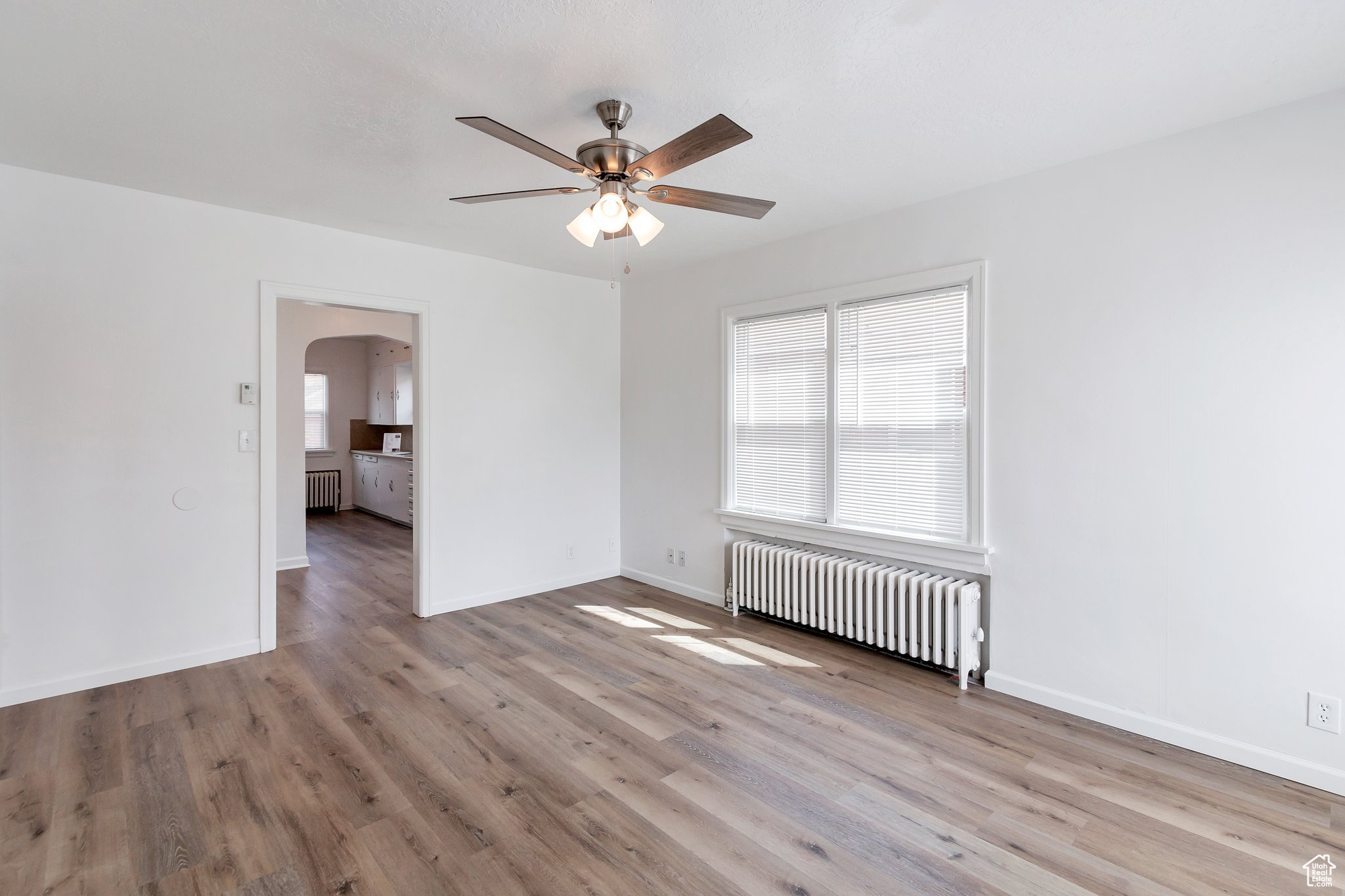 Unfurnished room featuring wood-type flooring, ceiling fan, and radiator heating unit