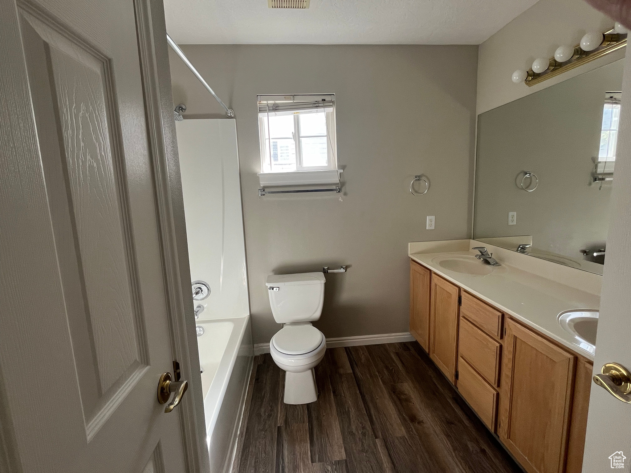 Full bathroom featuring double sink vanity, wood-type flooring, bathtub / shower combination, and toilet