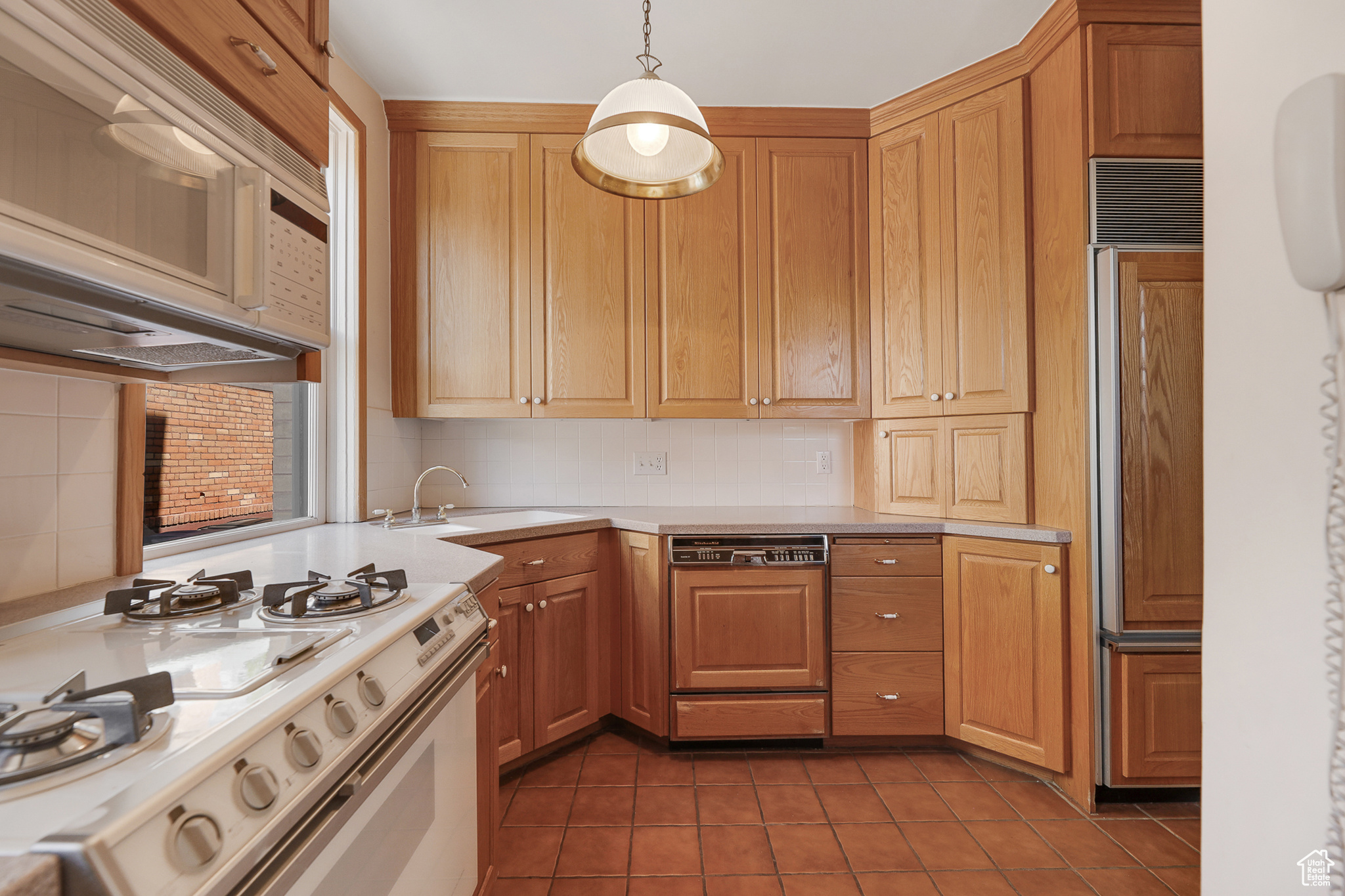 Kitchen with white appliances, tasteful backsplash, dark tile flooring, sink, and pendant lighting