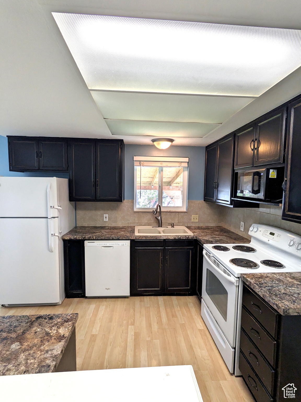 Kitchen with light hardwood / wood-style flooring, white appliances, tasteful backsplash, and sink