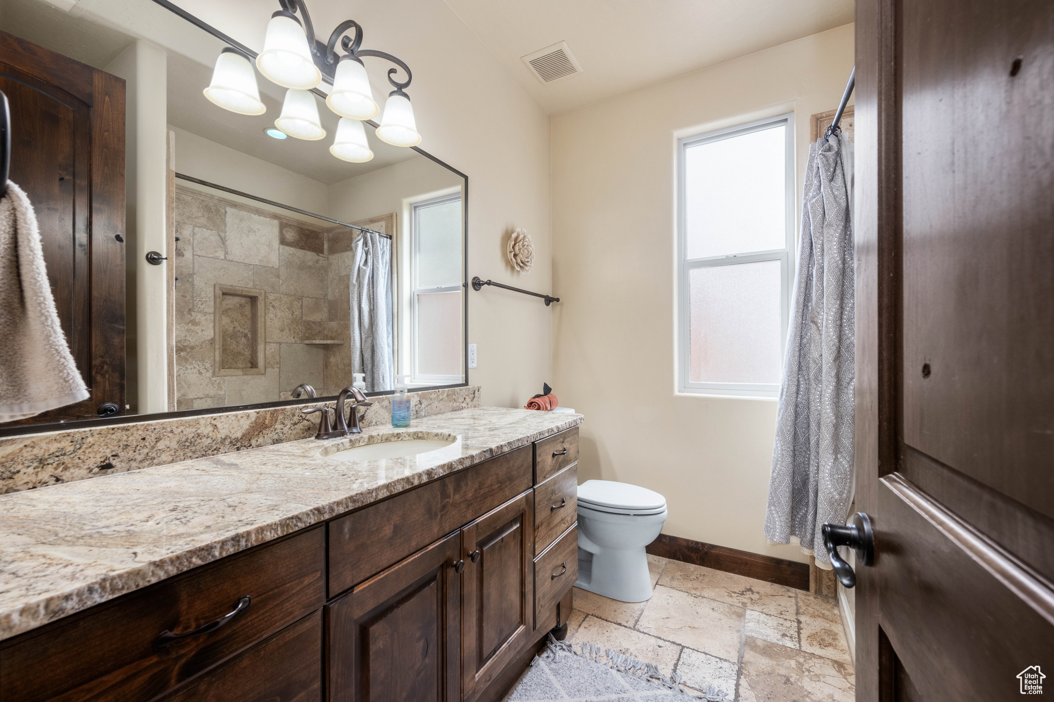 Bathroom with an inviting chandelier, toilet, tile floors, and vanity