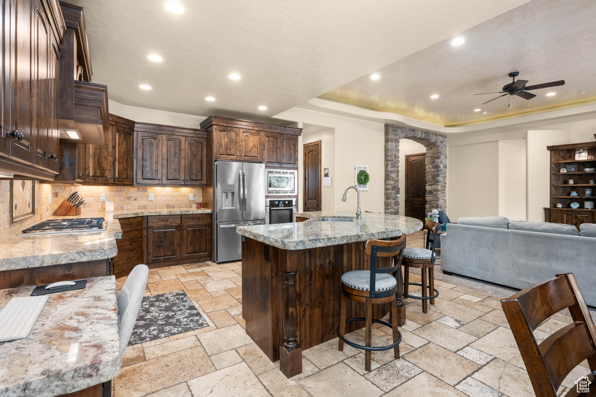 Kitchen with appliances with stainless steel finishes, ceiling fan, backsplash, a raised ceiling, and a center island with sink
