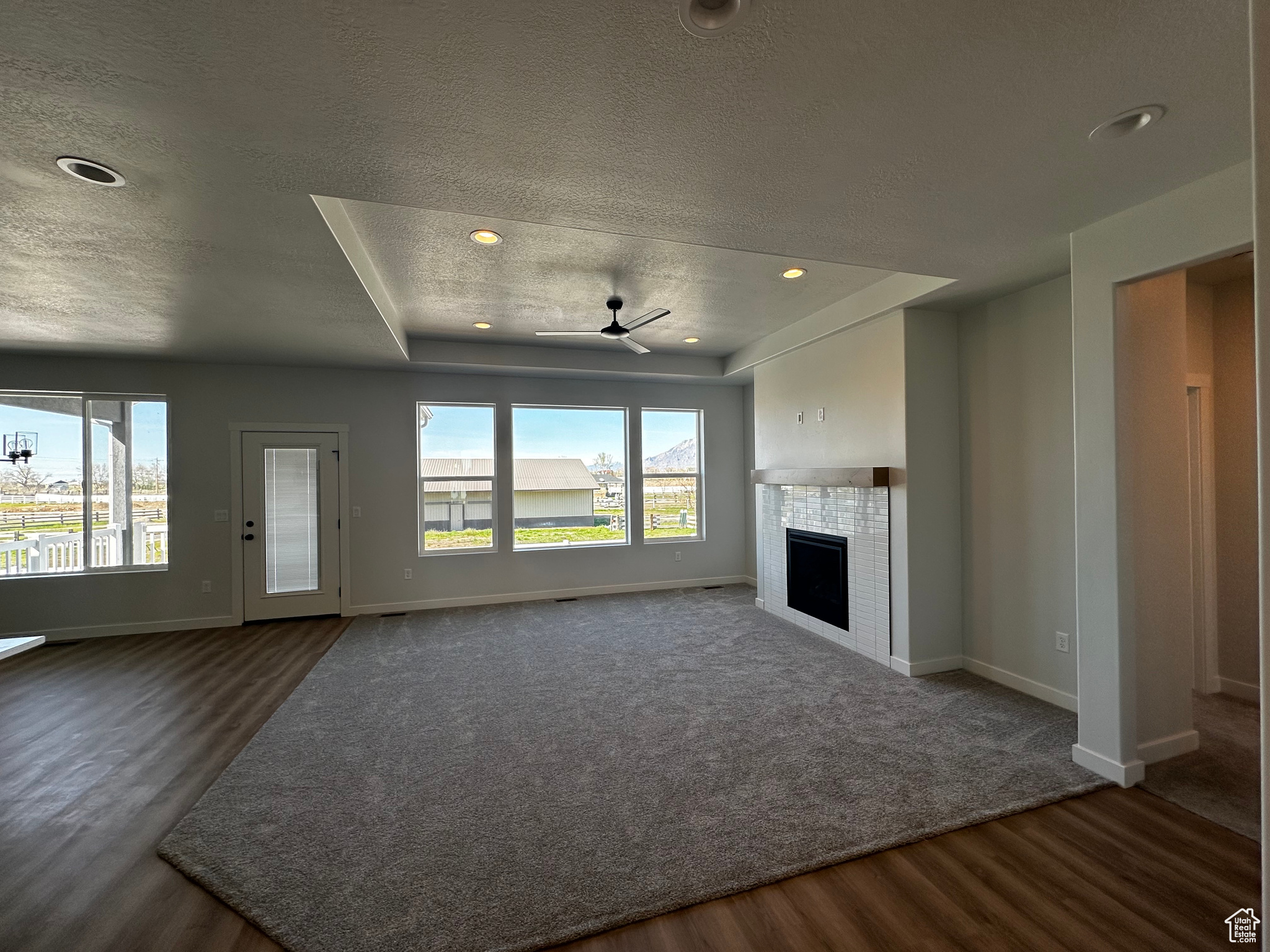 Unfurnished living room with a fireplace, dark colored carpet, ceiling fan, and a textured ceiling
