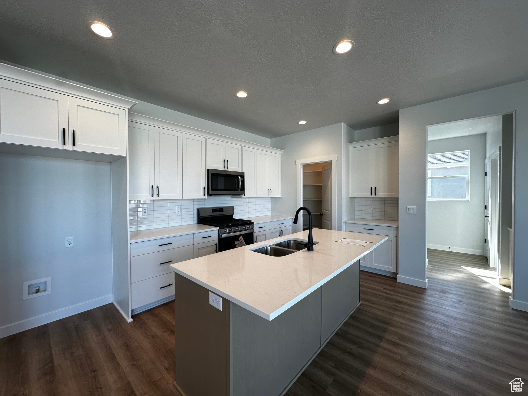 Kitchen featuring white cabinetry, appliances with stainless steel finishes, dark hardwood / wood-style floors, a kitchen island with sink, and sink
