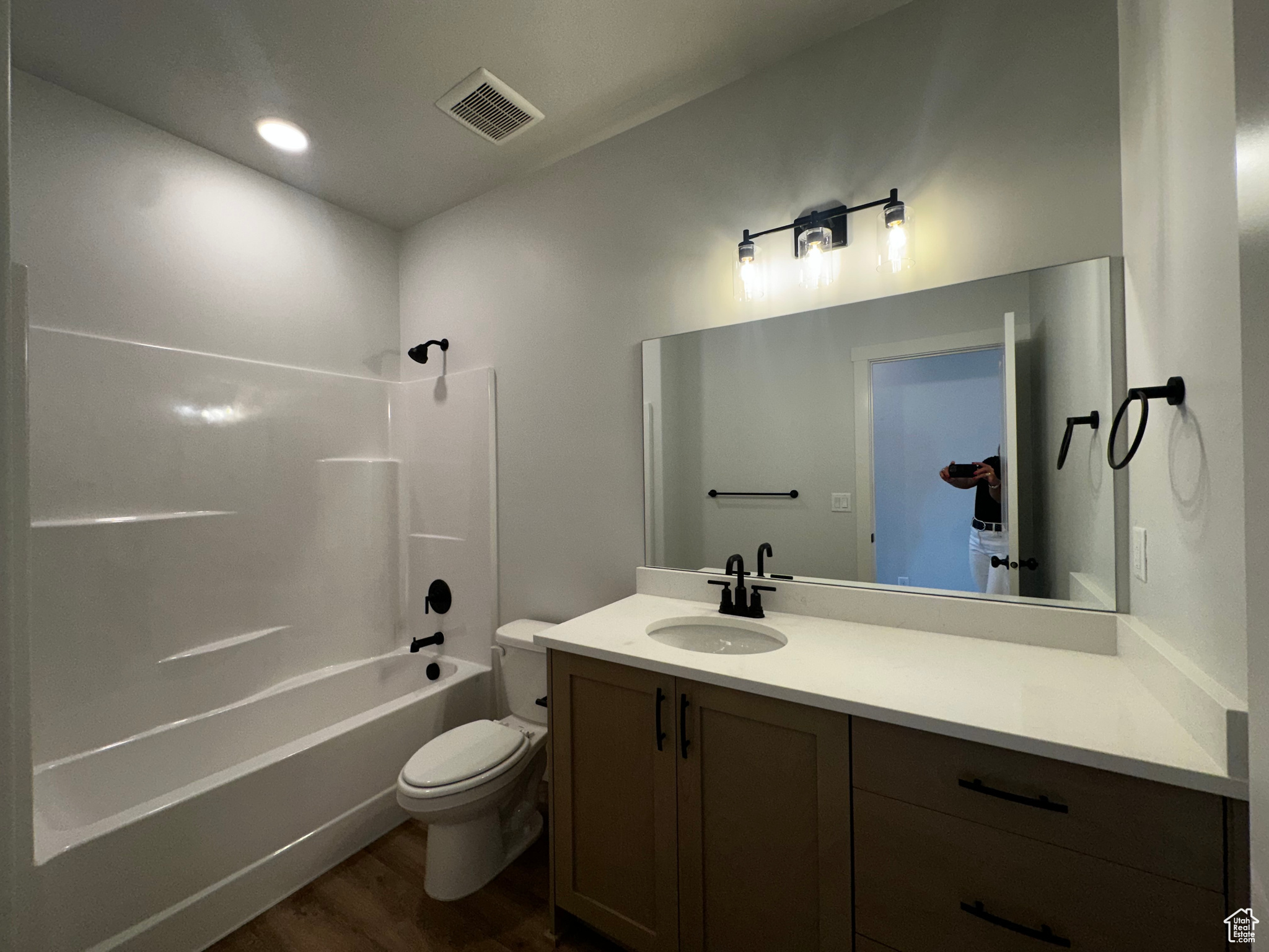 Full bathroom with wood-type flooring, shower / bath combination, vanity with extensive cabinet space, and toilet