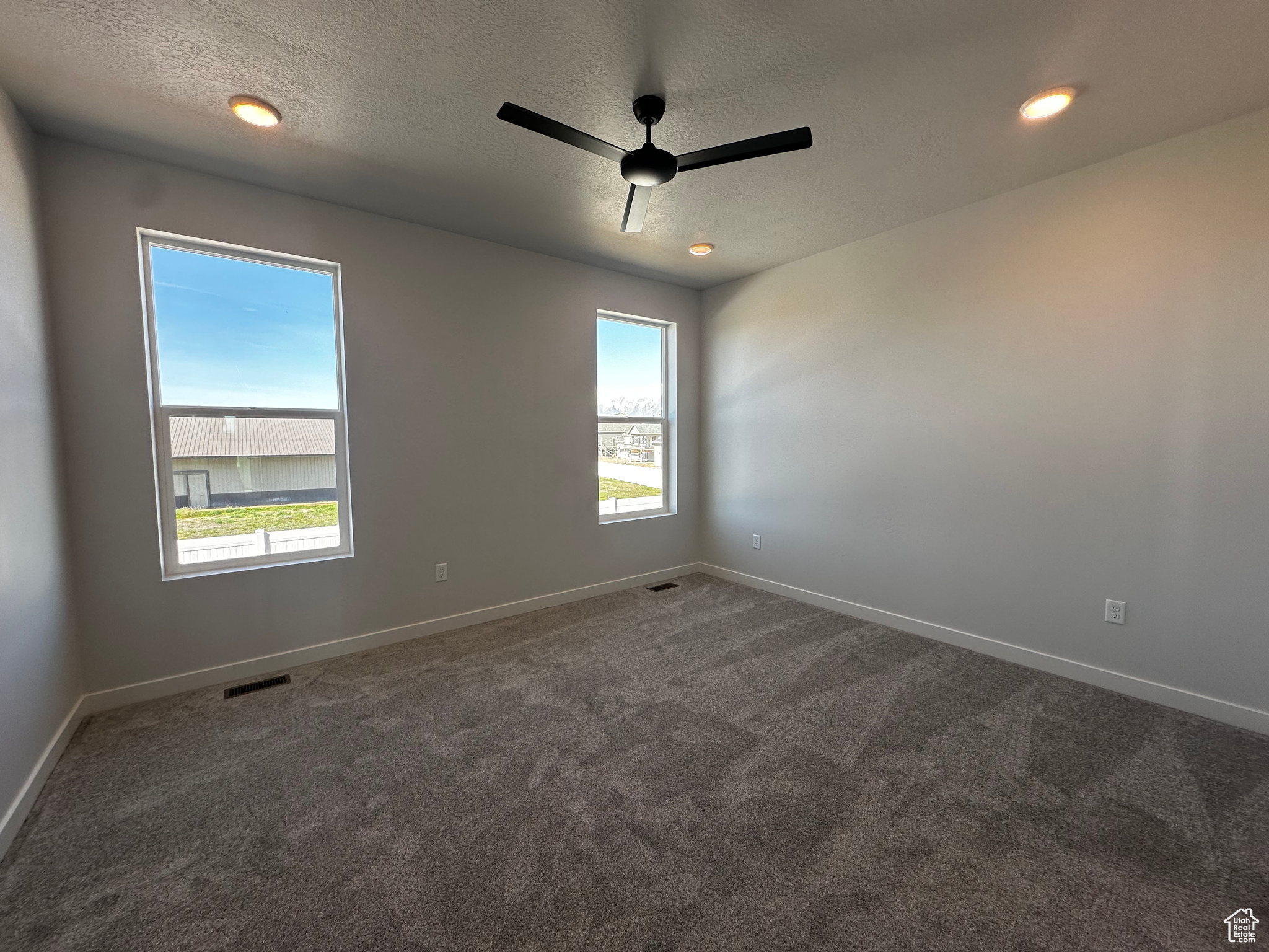 Empty room with ceiling fan, carpet floors, and a textured ceiling