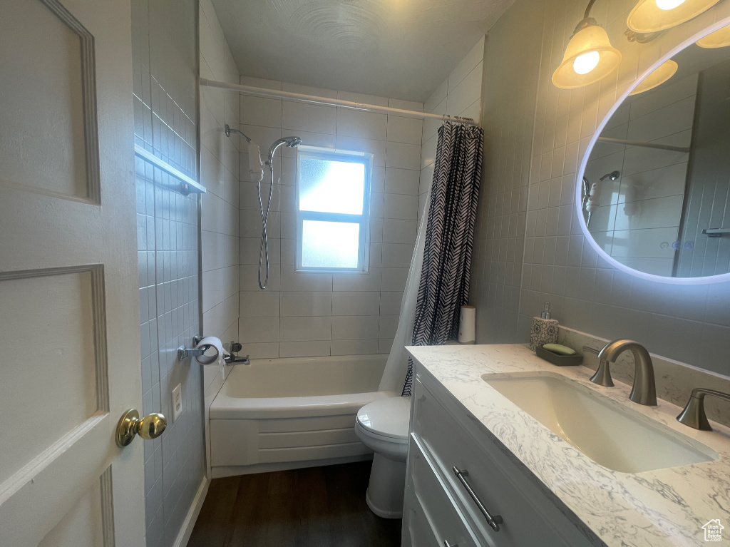 Full bathroom with vanity with extensive cabinet space, shower / bathtub combination with curtain, wood-type flooring, and toilet