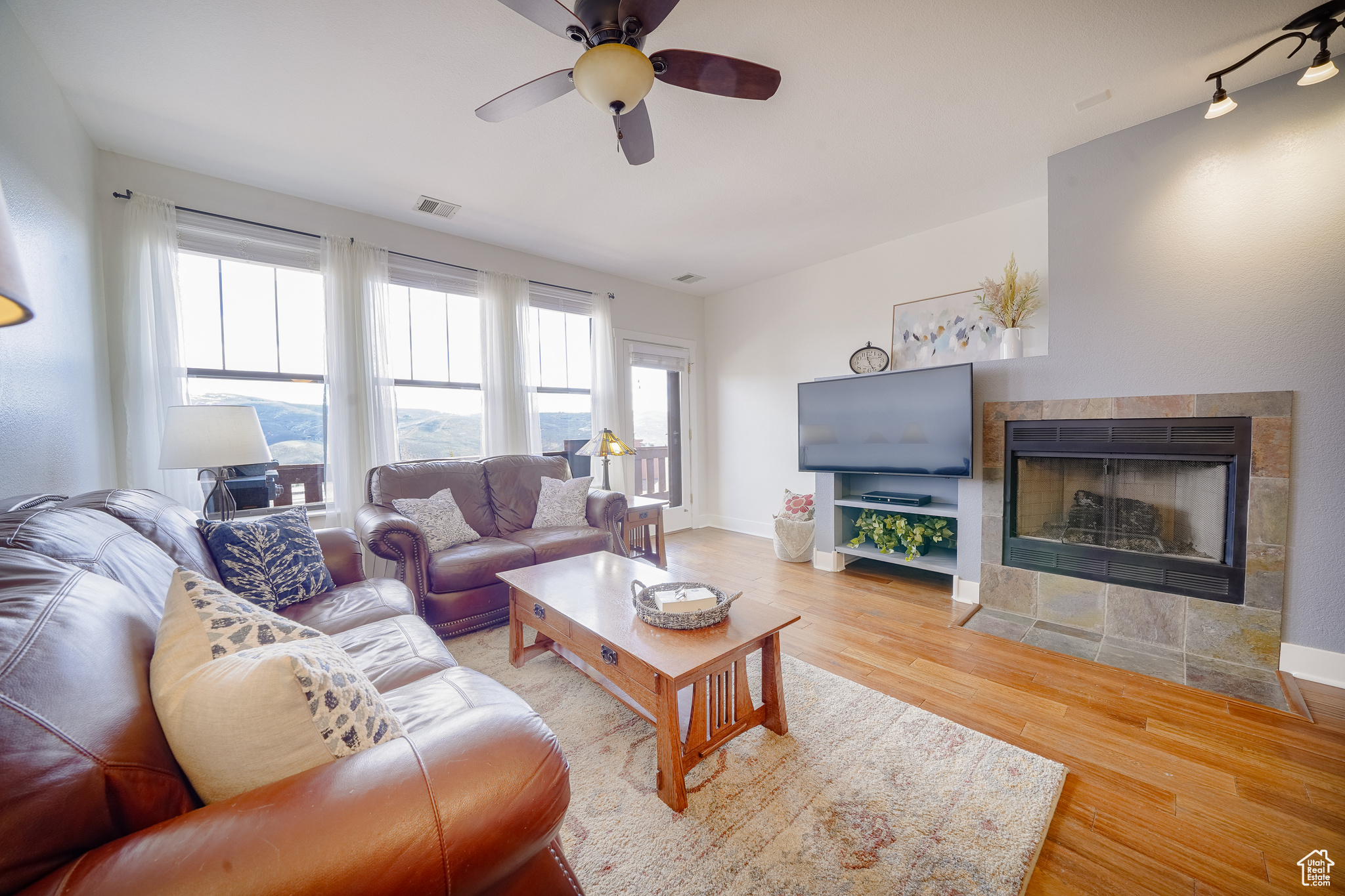 Living room featuring hardwood / wood-style floors, ceiling fan, and a tiled fireplace