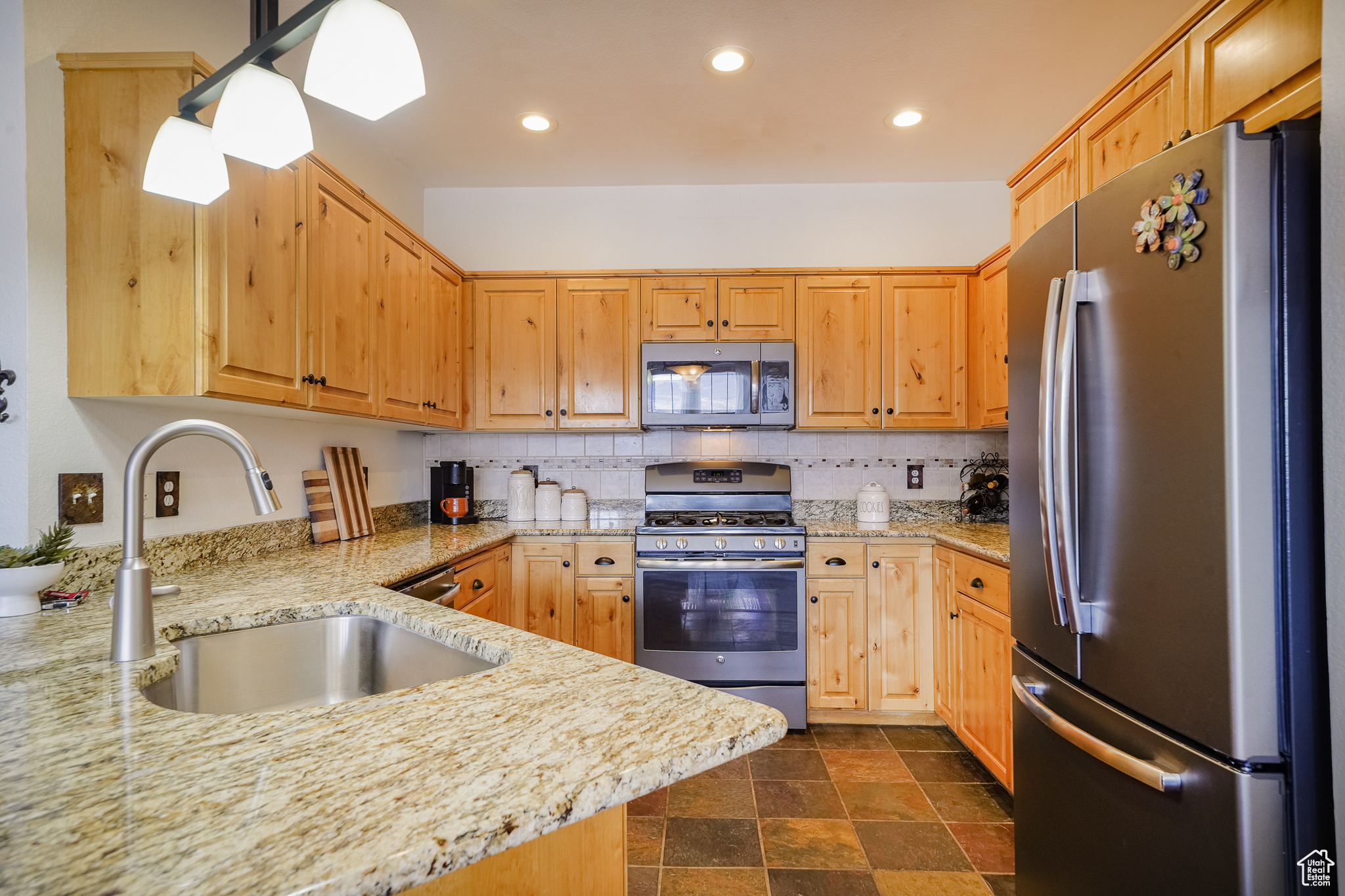 Kitchen featuring dark tile floors, tasteful backsplash, stainless steel refrigerator, sink, and range with gas cooktop