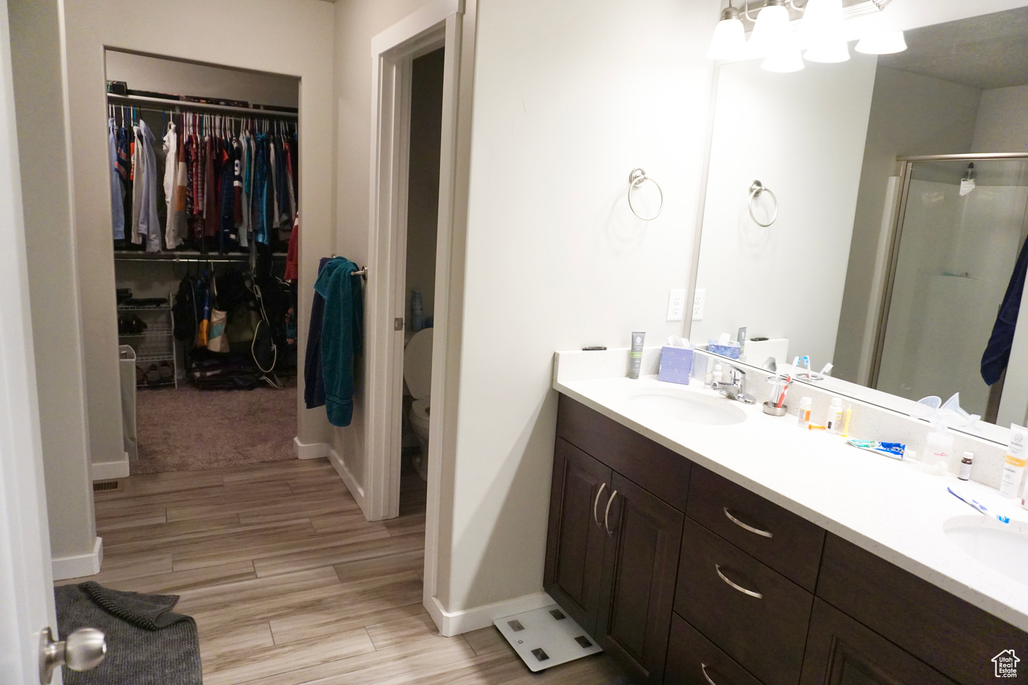 Bathroom with a shower, walk-in closet, dual sinks, vanity with extensive cabinet space, and toilet with door