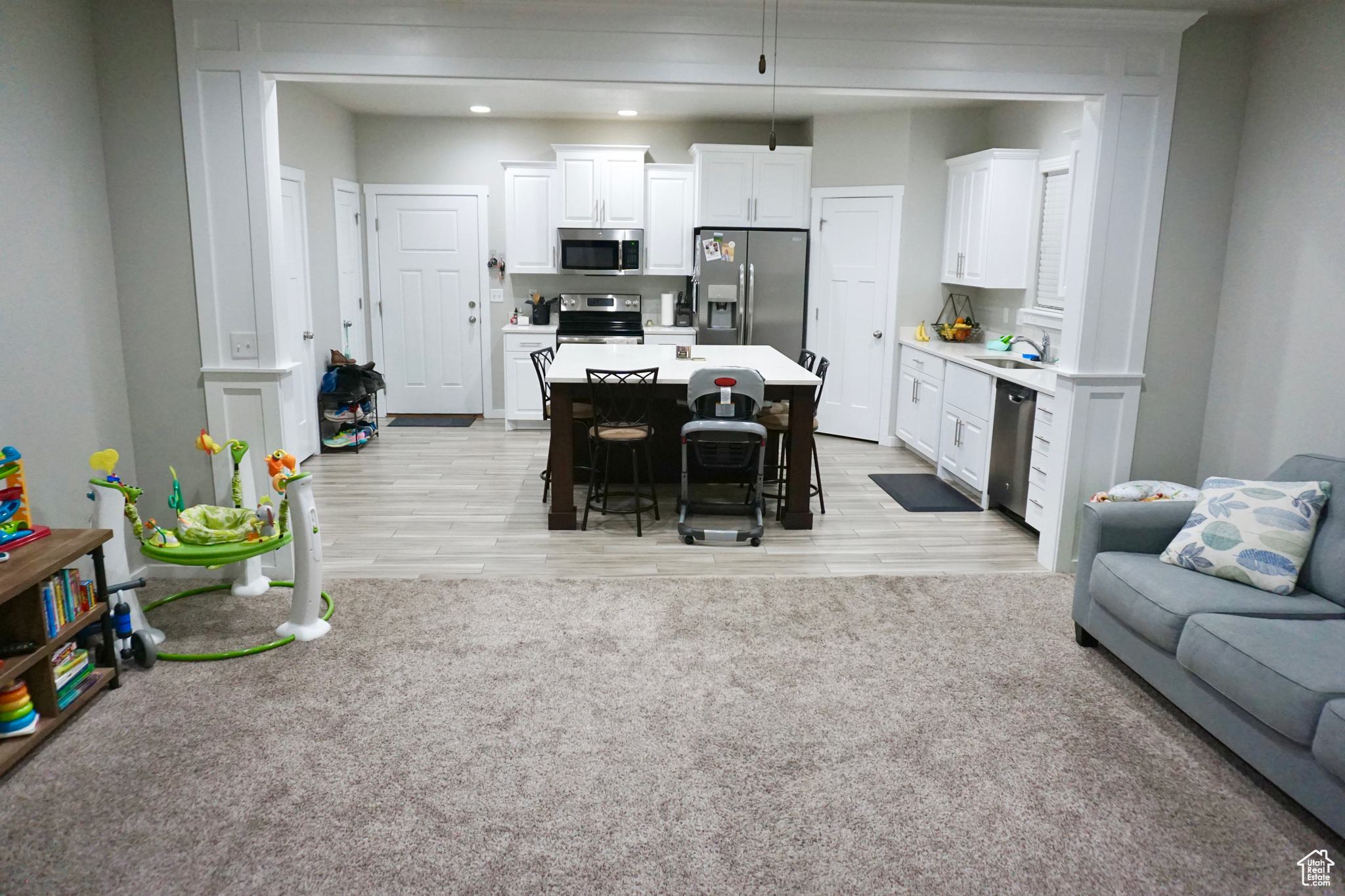Carpeted living room and tiled kitchen with stainless steel appliances, center island, white cabinets, and sink