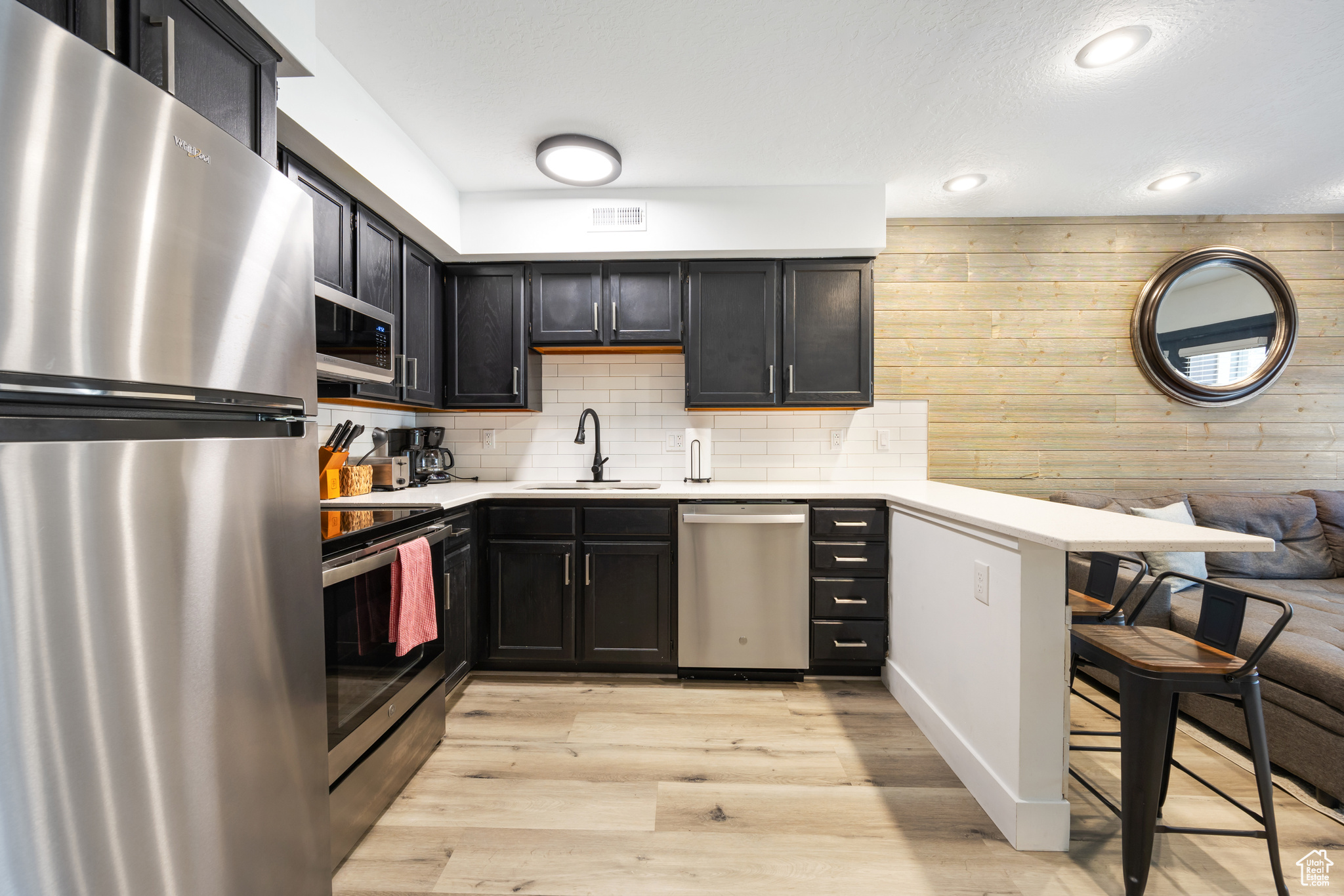 Kitchen featuring a kitchen bar, appliances with stainless steel finishes, light LVP flooring, tasteful backsplash, and sink