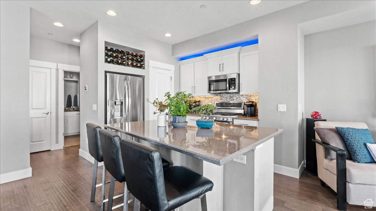 Kitchen featuring appliances with stainless steel finishes, a kitchen island, white cabinets, backsplash, and dark hardwood / wood-style floors