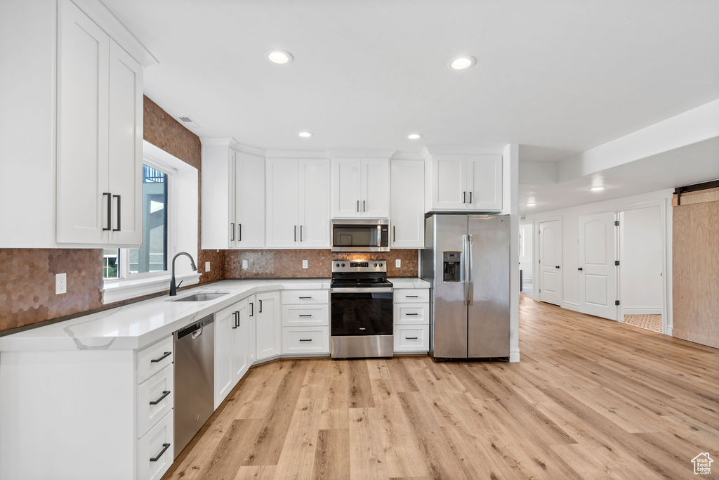 Kitchen featuring appliances with stainless steel finishes, light hardwood / wood-style floors, white cabinets, and sink