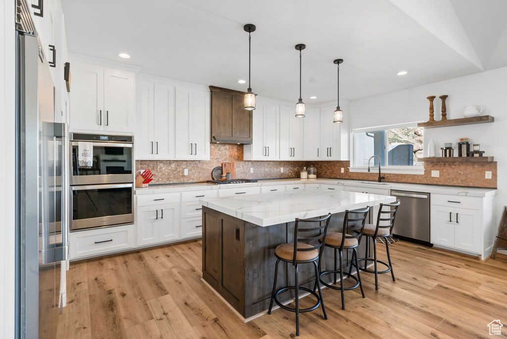 Kitchen featuring light wood-type flooring, stainless steel appliances, light stone counters, a kitchen island, and tasteful backsplash