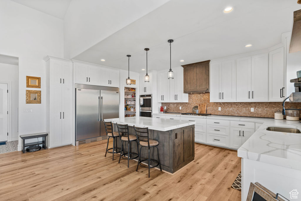 Kitchen with appliances with stainless steel finishes, backsplash, white cabinets, a center island, and light wood-type flooring