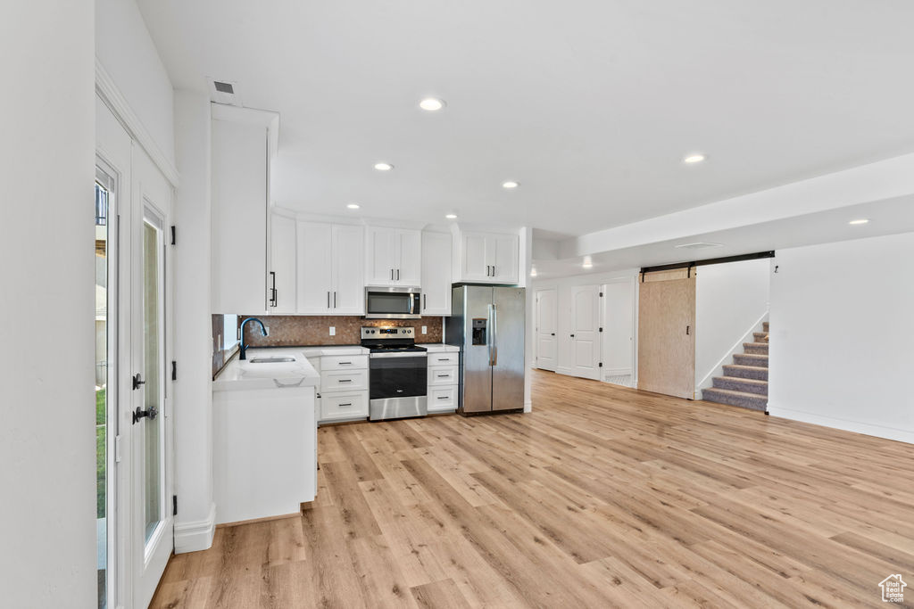 Kitchen featuring light hardwood / wood-style flooring, white cabinetry, backsplash, appliances with stainless steel finishes, and sink
