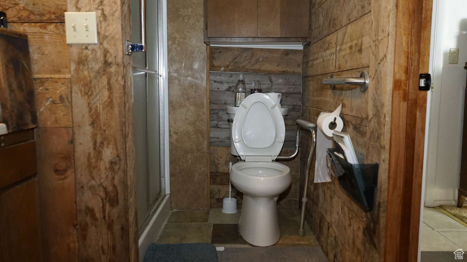 Bathroom featuring a shower with shower door, toilet, and tile flooring