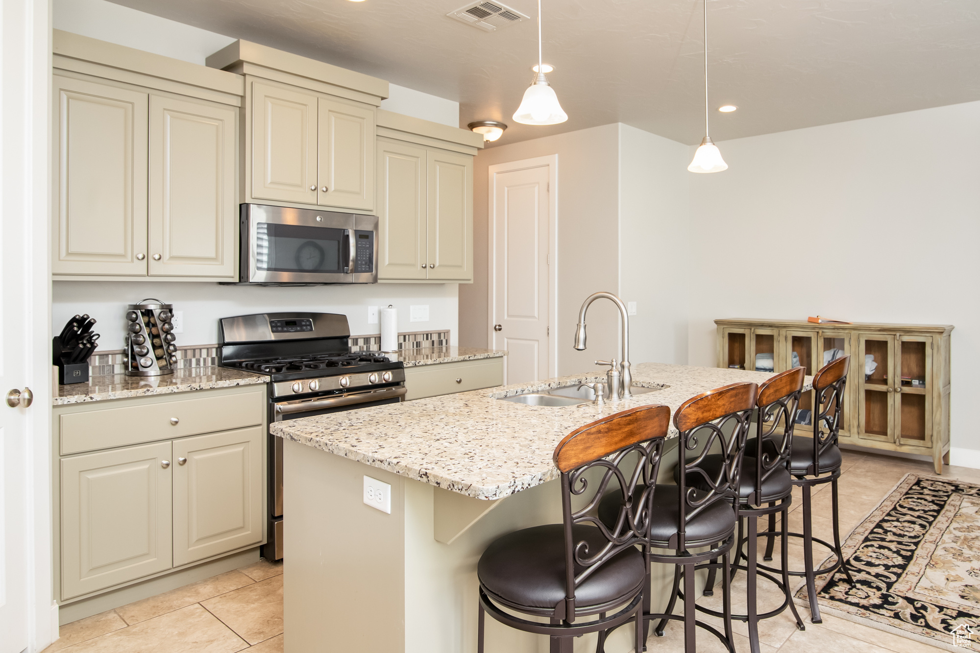 Kitchen with pendant lighting, appliances with stainless steel finishes, light tile floors, a center island with granite countertops, and cream cabinetry