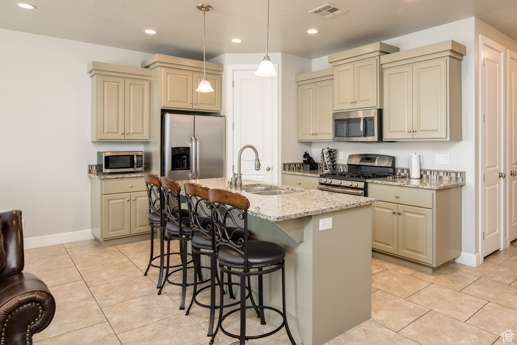 Kitchen featuring stainless steel appliances, a kitchen island with granite countertops, sink, pendant lighting, and light tile floors