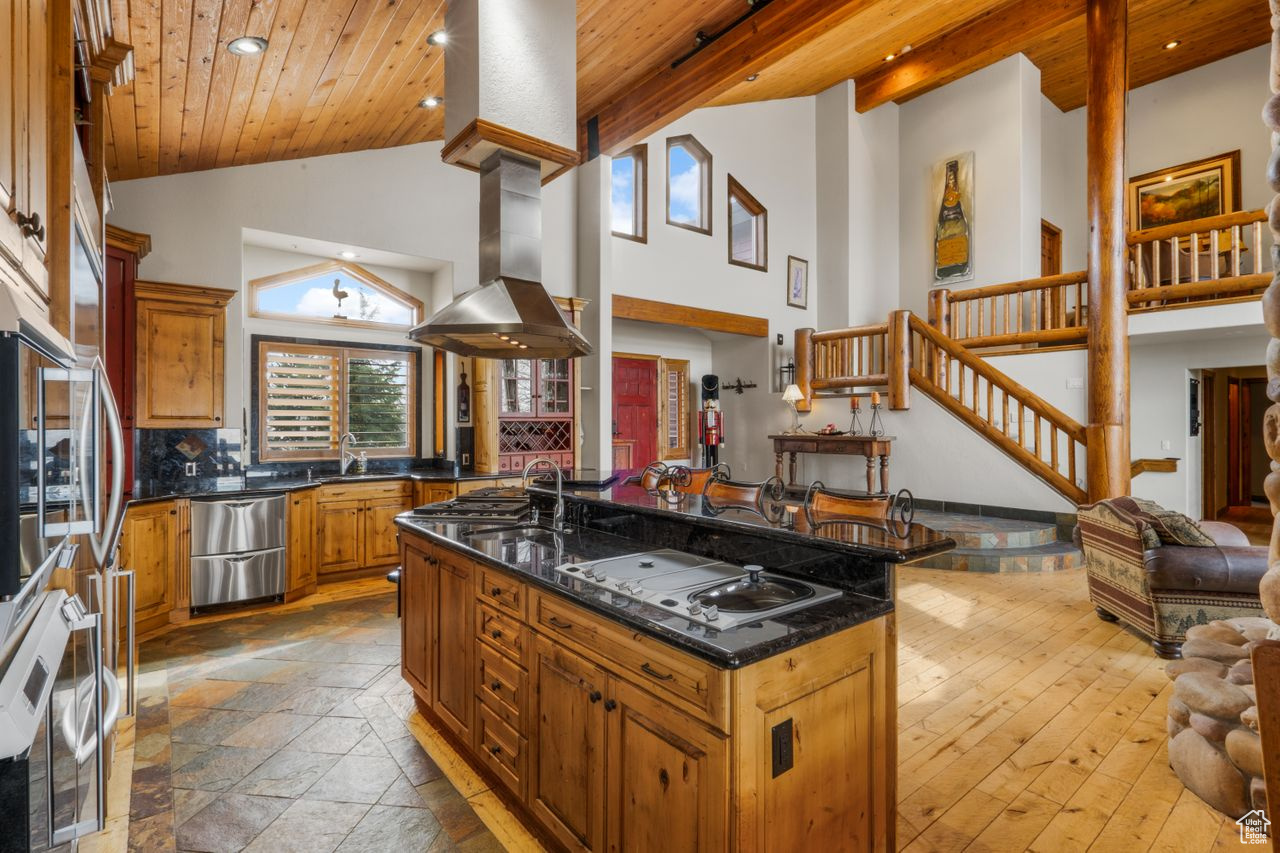 Kitchen featuring light hardwood / wood-style floors, tasteful backsplash, island range hood, wood ceiling, and a center island with sink
