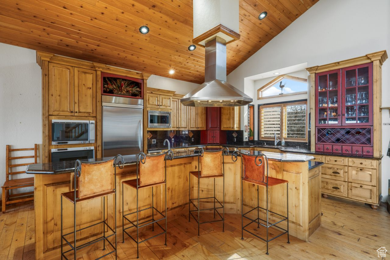 Kitchen with built in appliances, light hardwood / wood-style floors, island range hood, wood ceiling, and a center island