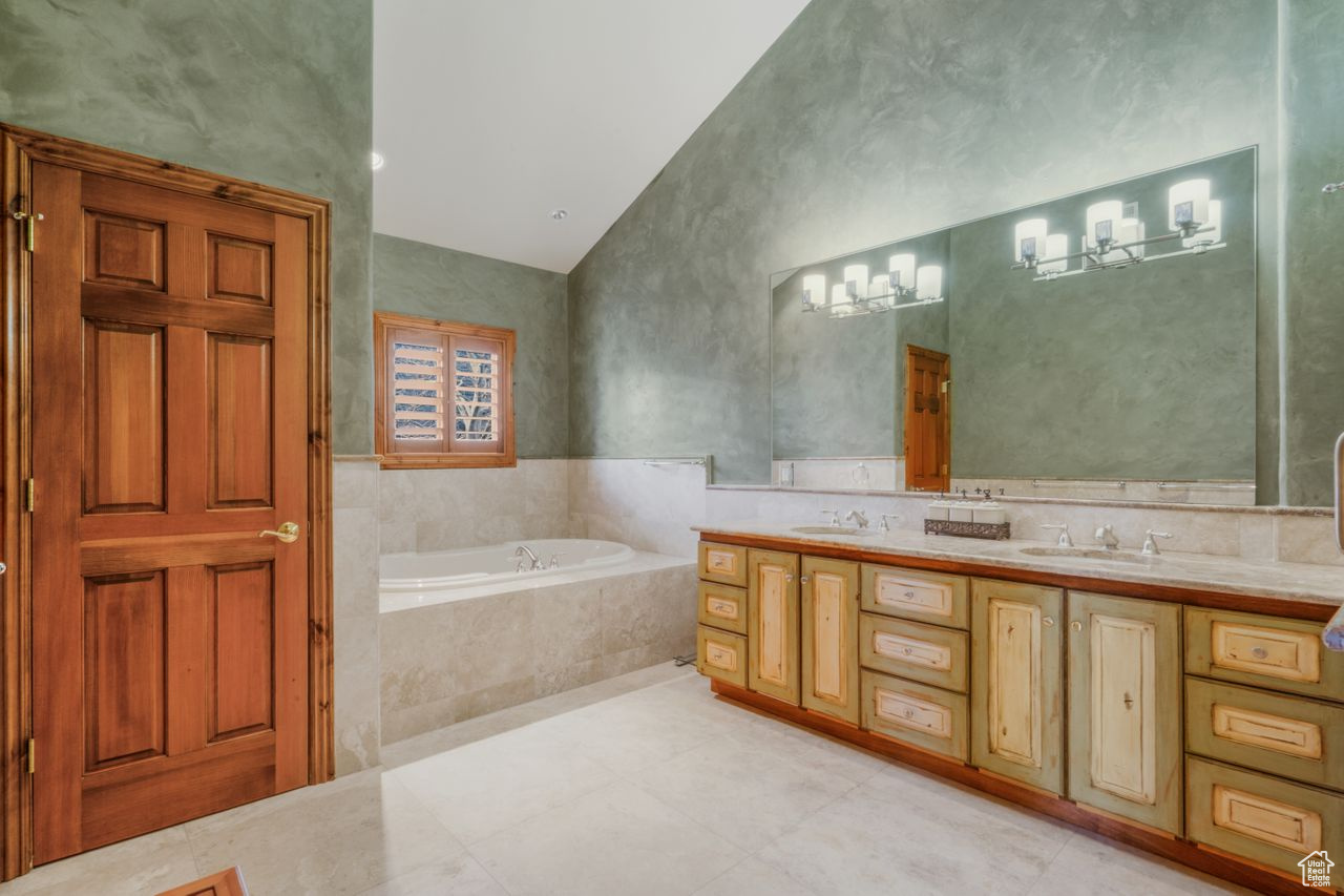 Bathroom featuring dual sinks, oversized vanity, vaulted ceiling, and tiled tub