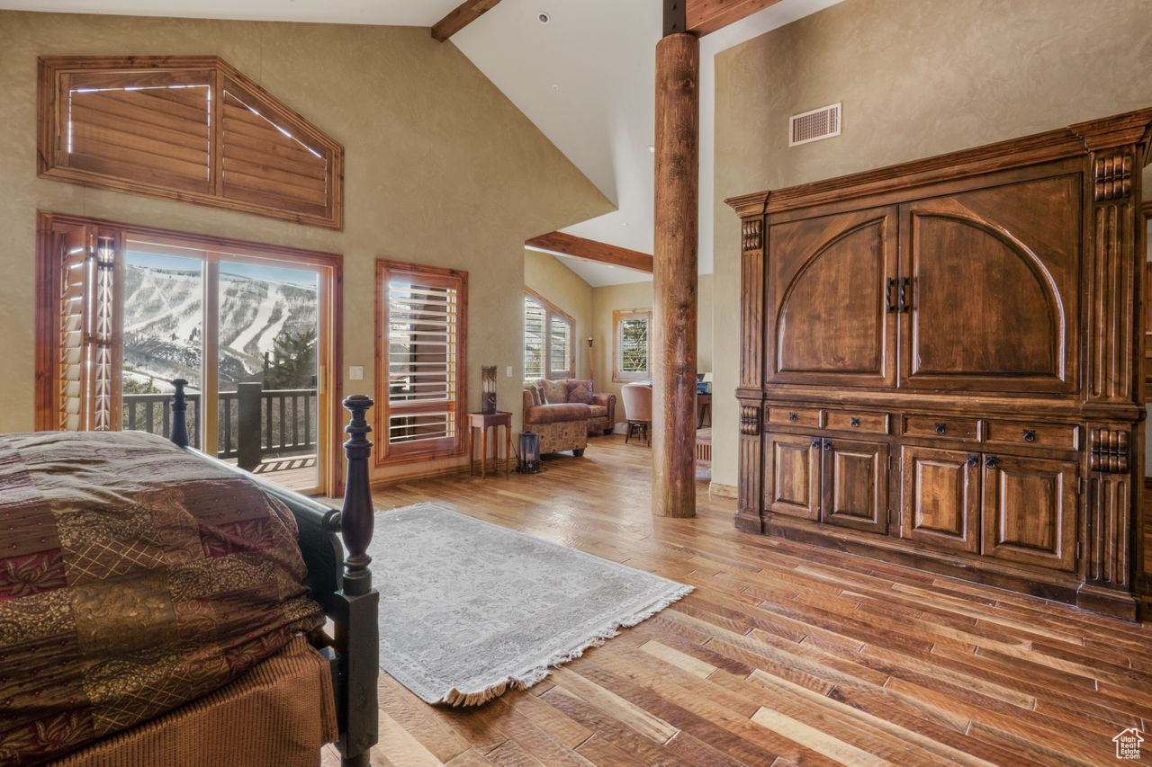 Bedroom with a mountain view, high vaulted ceiling, beam ceiling, access to outside, and hardwood / wood-style flooring