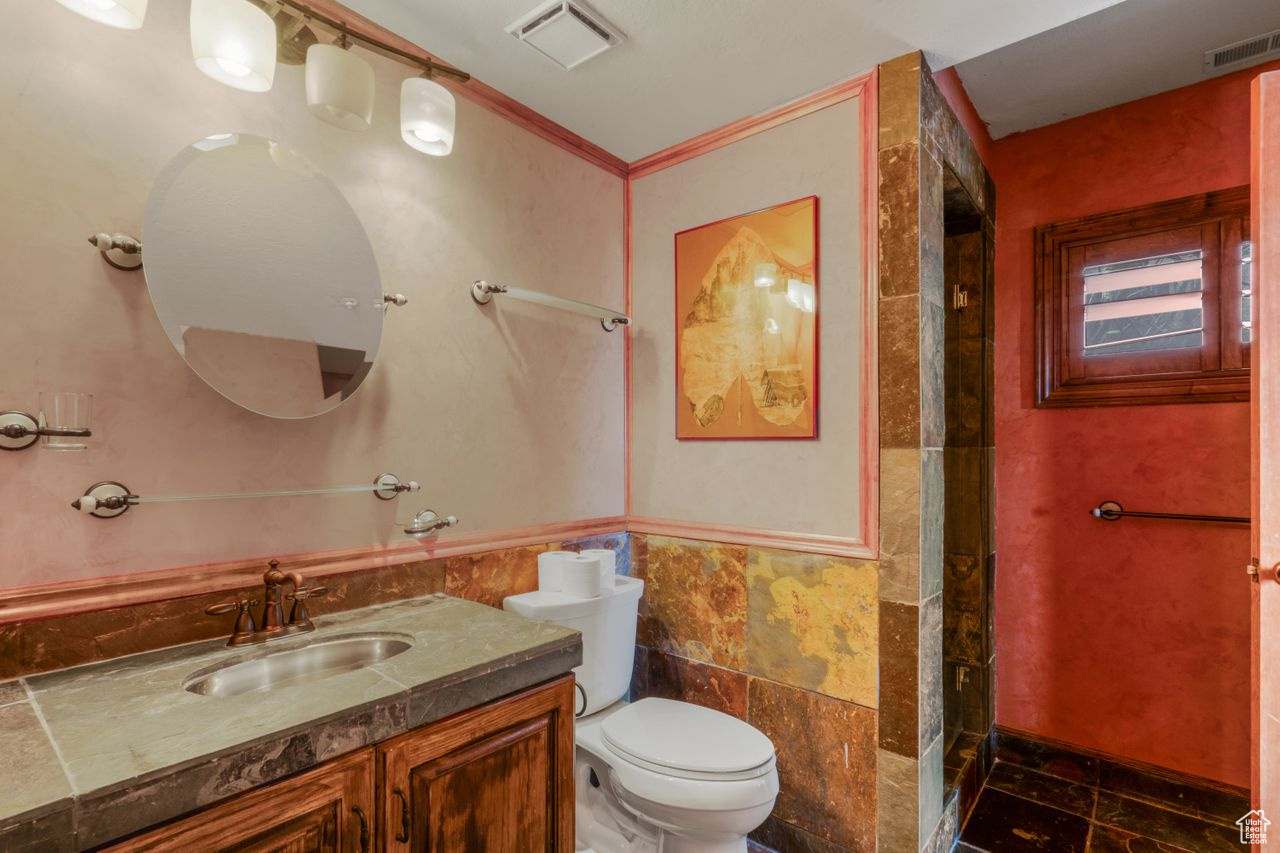 Bathroom with tile floors, vanity, tile walls, ornamental molding, and toilet