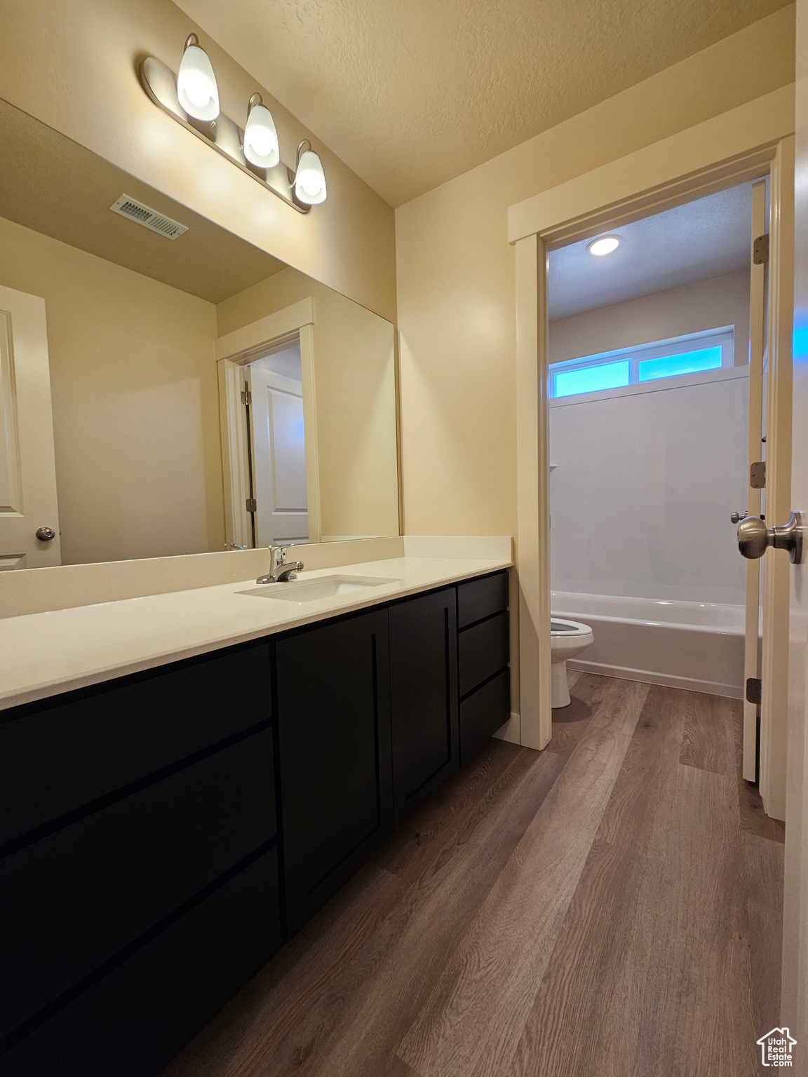 Full bathroom featuring vanity, hardwood / wood-style flooring, shower / bath combination, toilet, and a textured ceiling