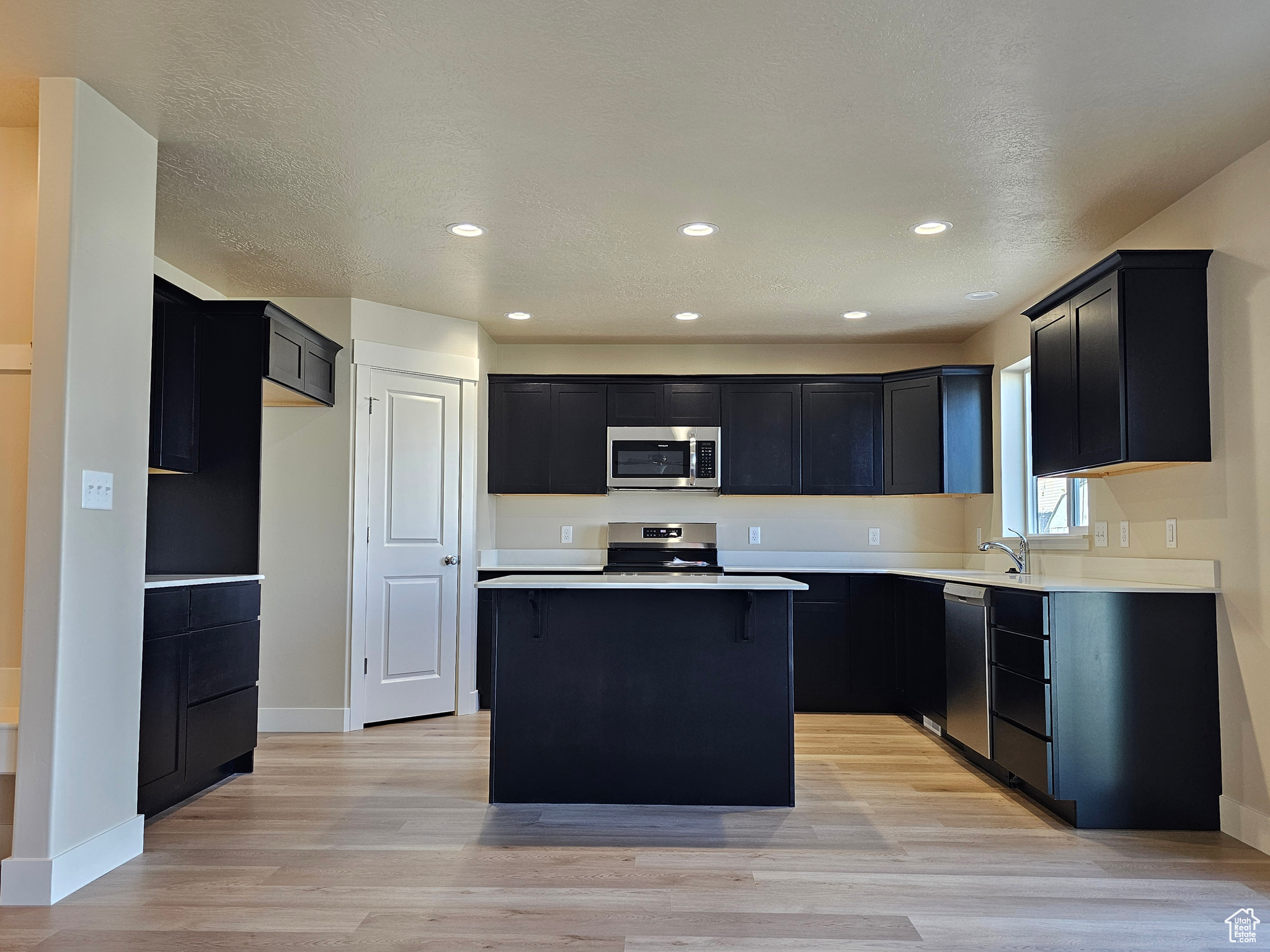 Kitchen with a kitchen bar, appliances with stainless steel finishes, light wood-type flooring, and a kitchen island