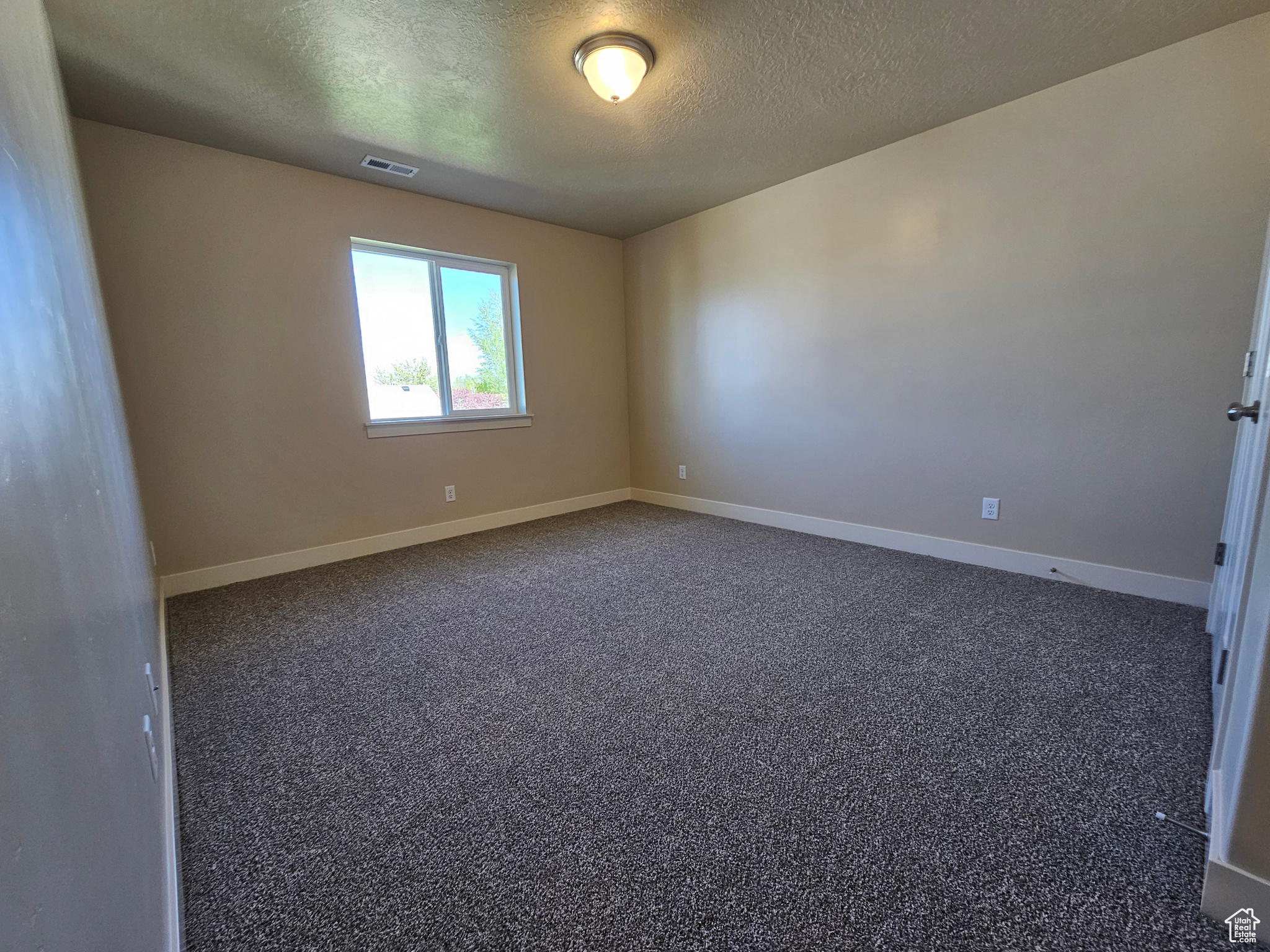 Spare room featuring a textured ceiling and dark colored carpet