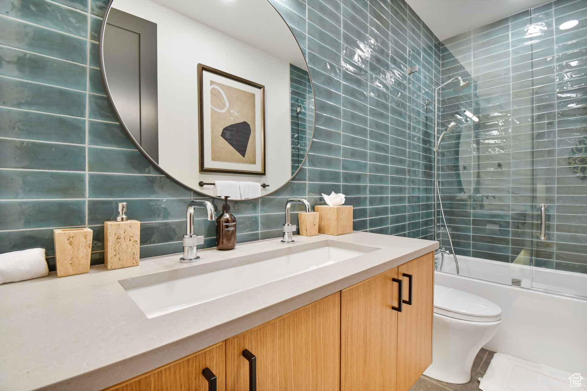 Full bathroom with tile walls, shower / bath combination with glass door, vanity, and toilet