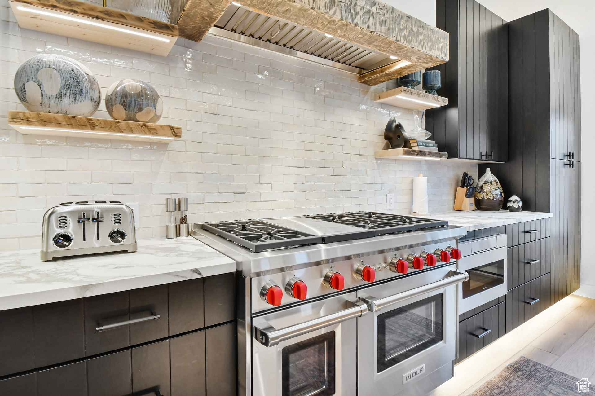 Kitchen with backsplash, double oven range, hardwood / wood-style floors, and light stone countertops