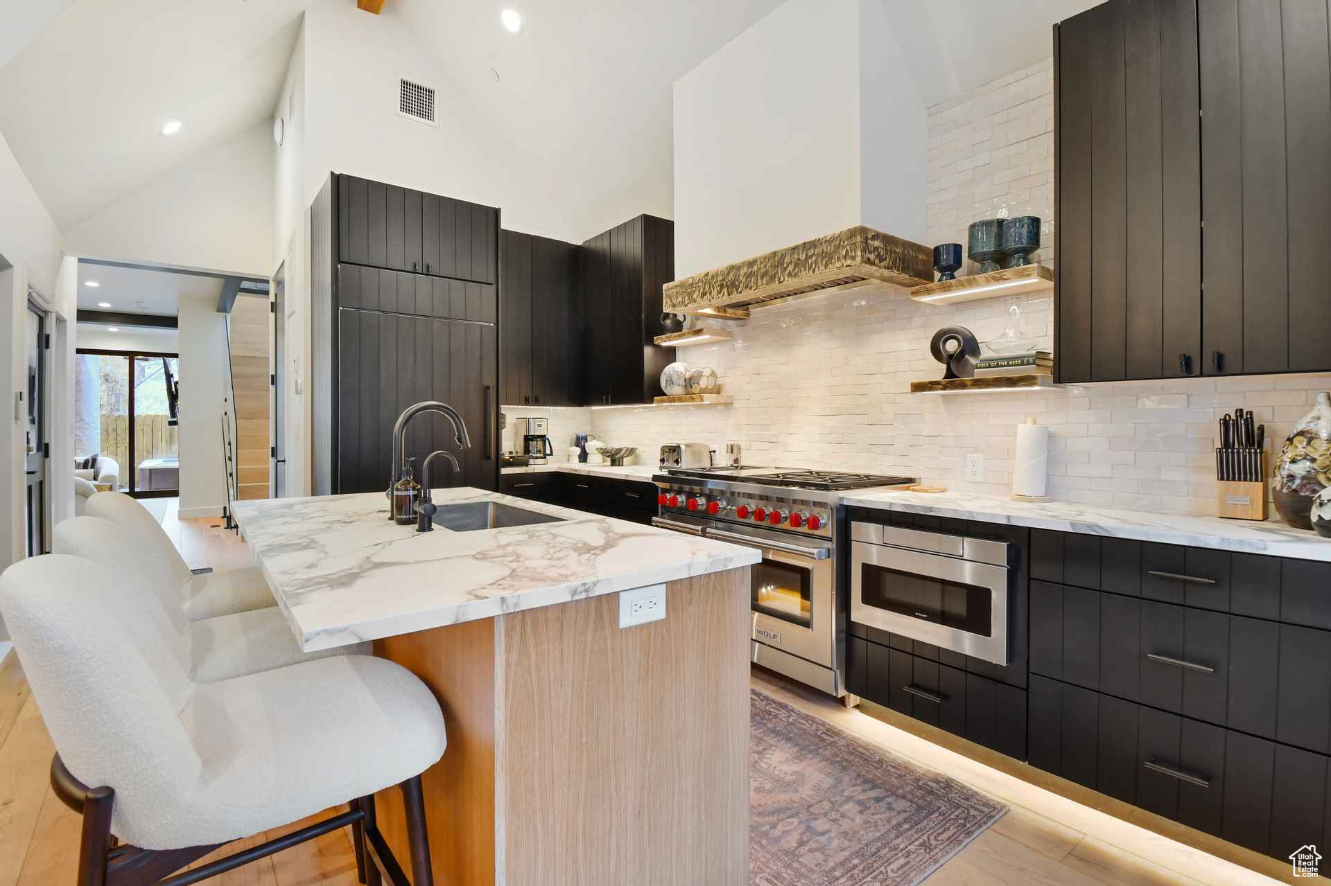 Kitchen with premium range hood, backsplash, double oven range, a center island with sink, and light hardwood / wood-style floors