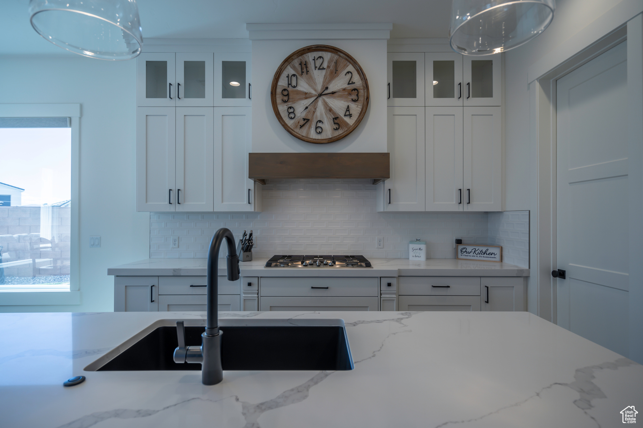 Kitchen featuring light stone counters, stainless steel gas stovetop, white cabinets, sink, and tasteful backsplash