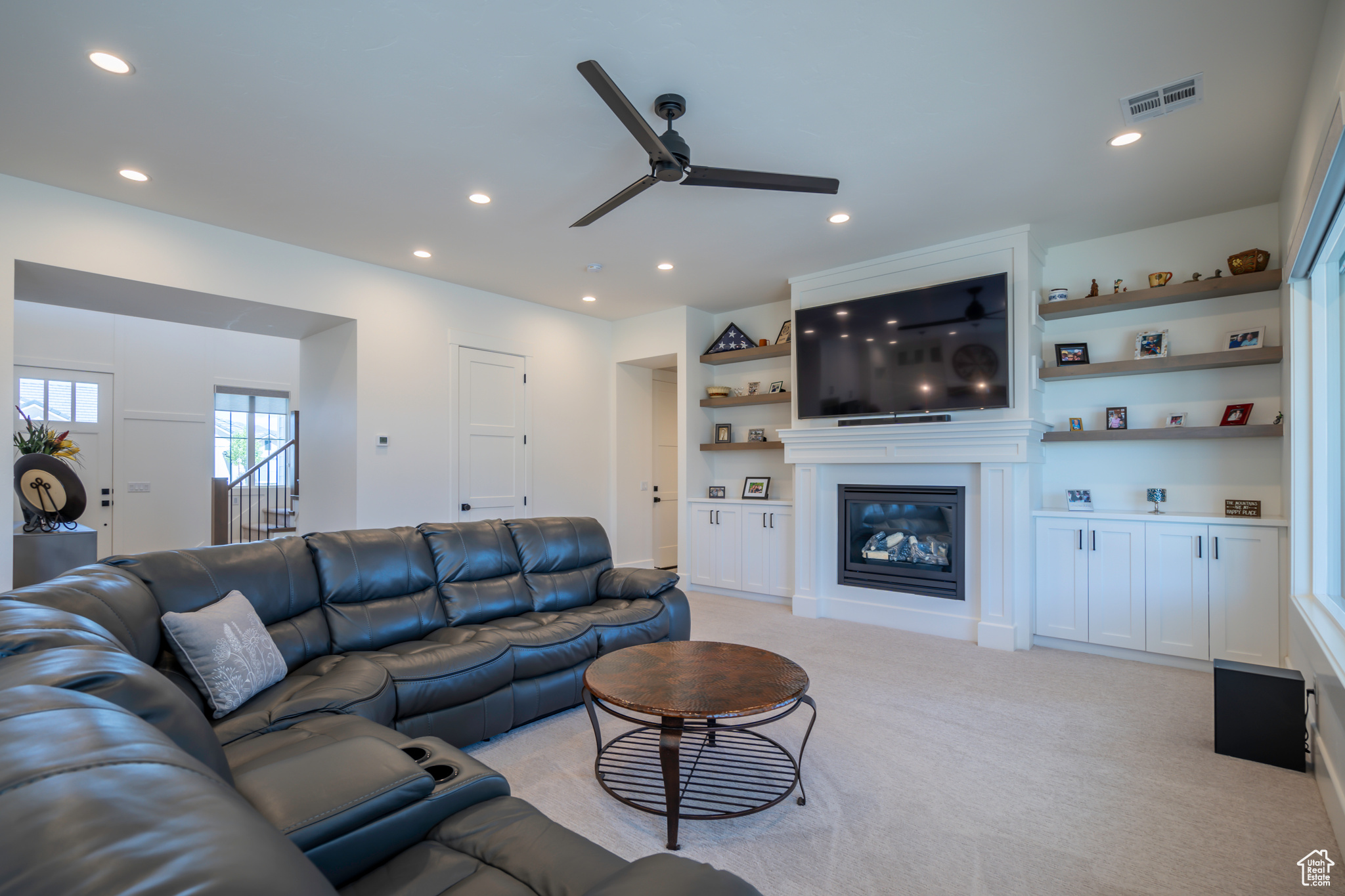 Carpeted living room with built in features and ceiling fan