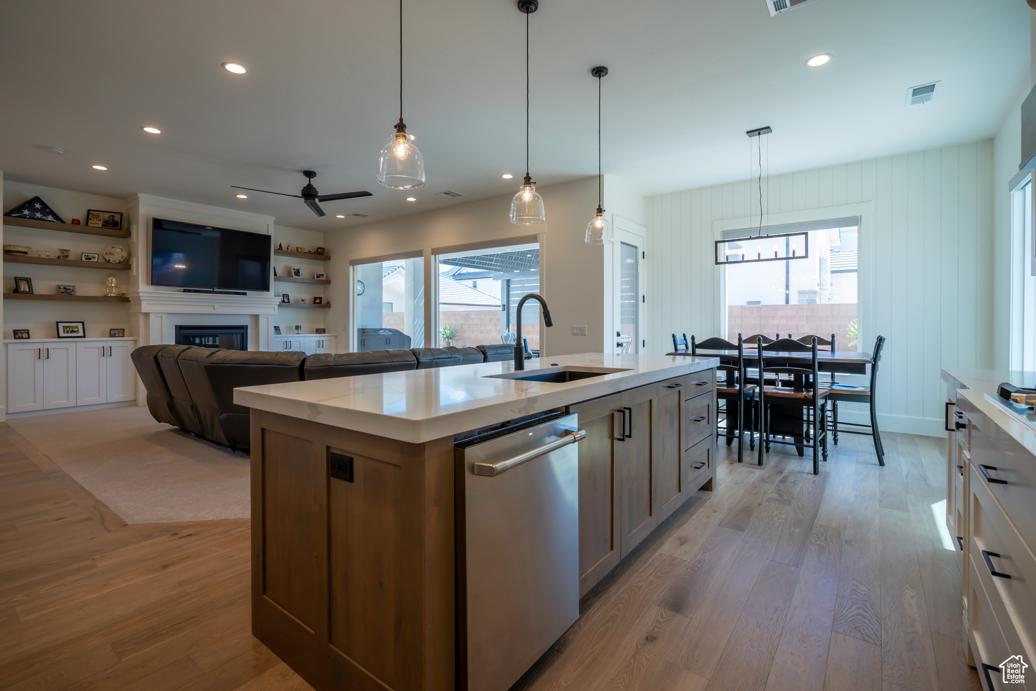 Kitchen with a large fireplace, light hardwood / wood-style flooring, sink, a center island with sink, and stainless steel dishwasher
