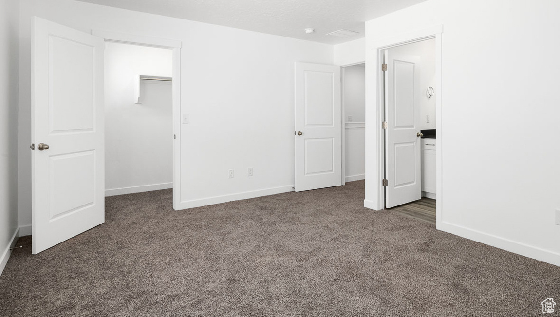 Unfurnished bedroom with dark colored carpet, ensuite bath, a closet, and a walk in closet