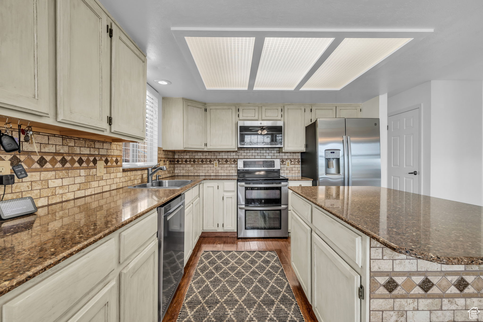 Kitchen featuring stainless steel appliances, tasteful backsplash, dark wood-type flooring, dark stone counters, and sink