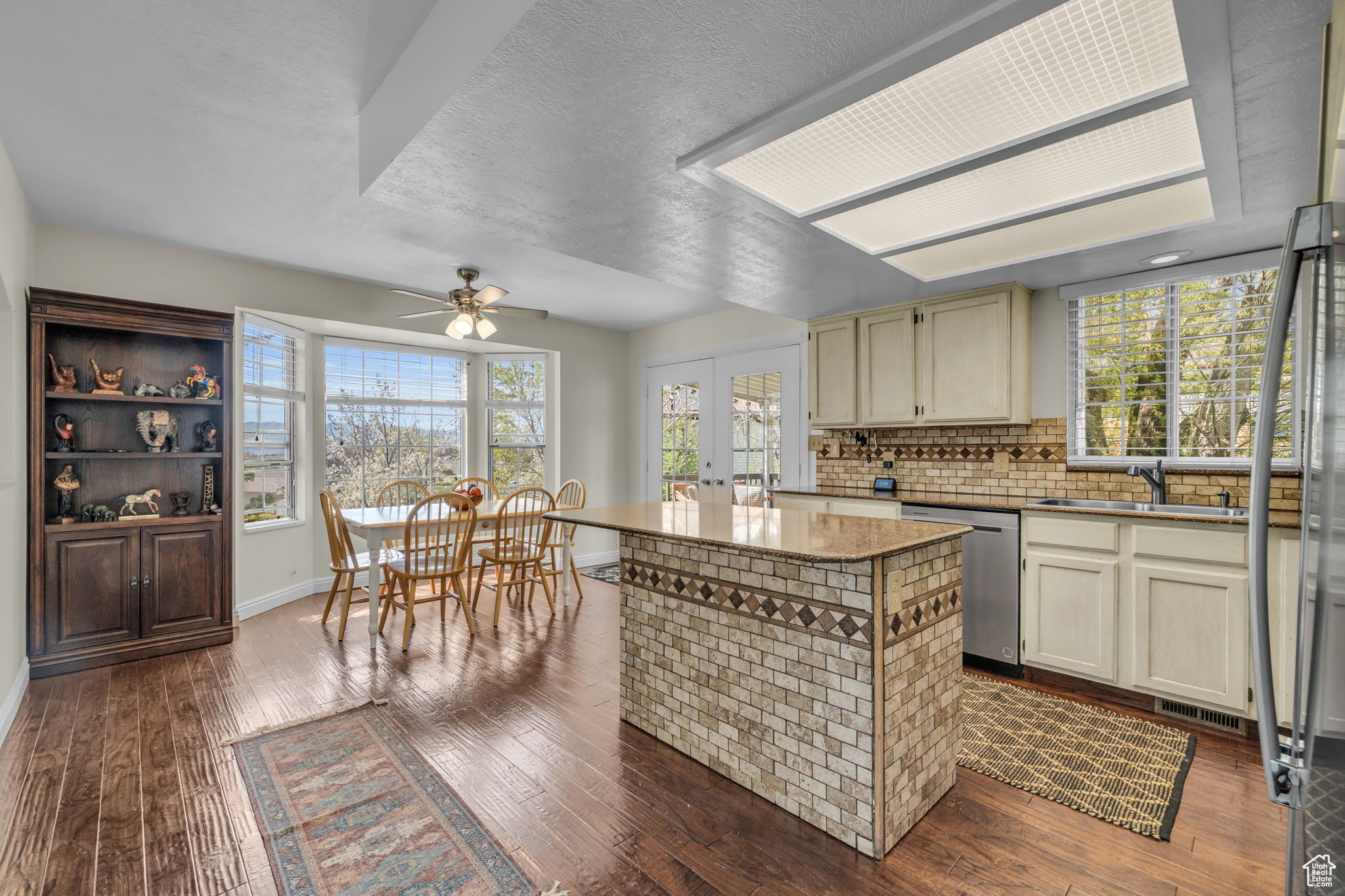 Kitchen with cream cabinets, backsplash, ceiling fan, dark wood-type flooring, and stainless steel dishwasher