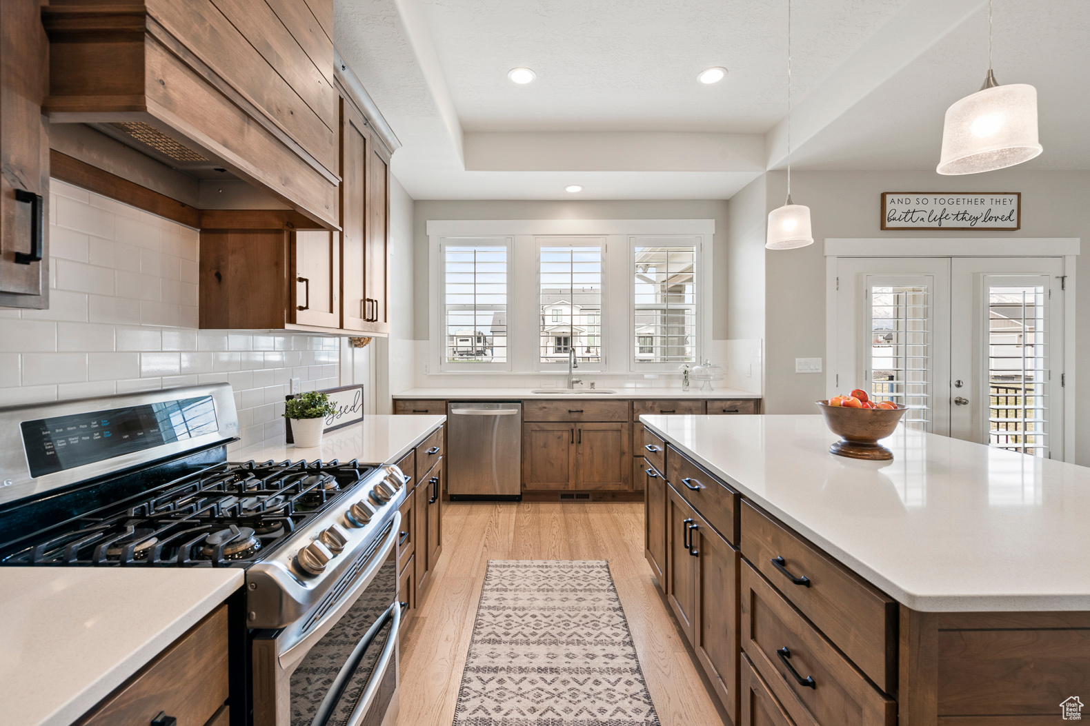 Kitchen featuring premium range hood, decorative light fixtures, backsplash, stainless steel appliances, and light hardwood / wood-style floors