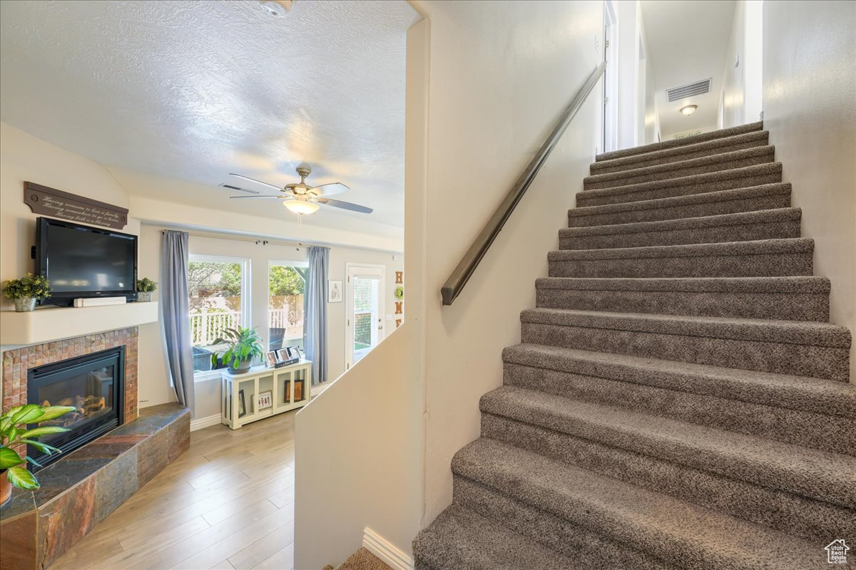 Stairs with a textured ceiling, hardwood / wood-style floors, ceiling fan, and a tiled fireplace