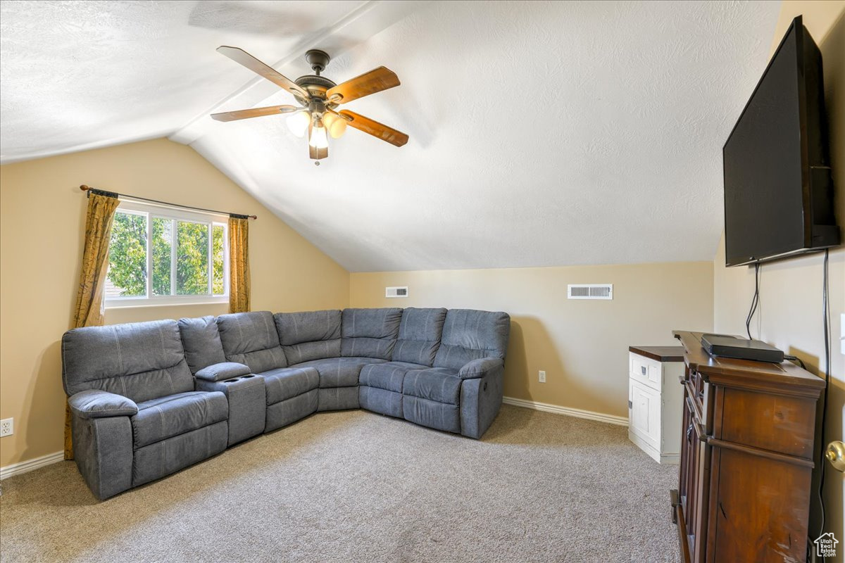 Carpeted living room featuring lofted ceiling, ceiling fan, and a textured ceiling
