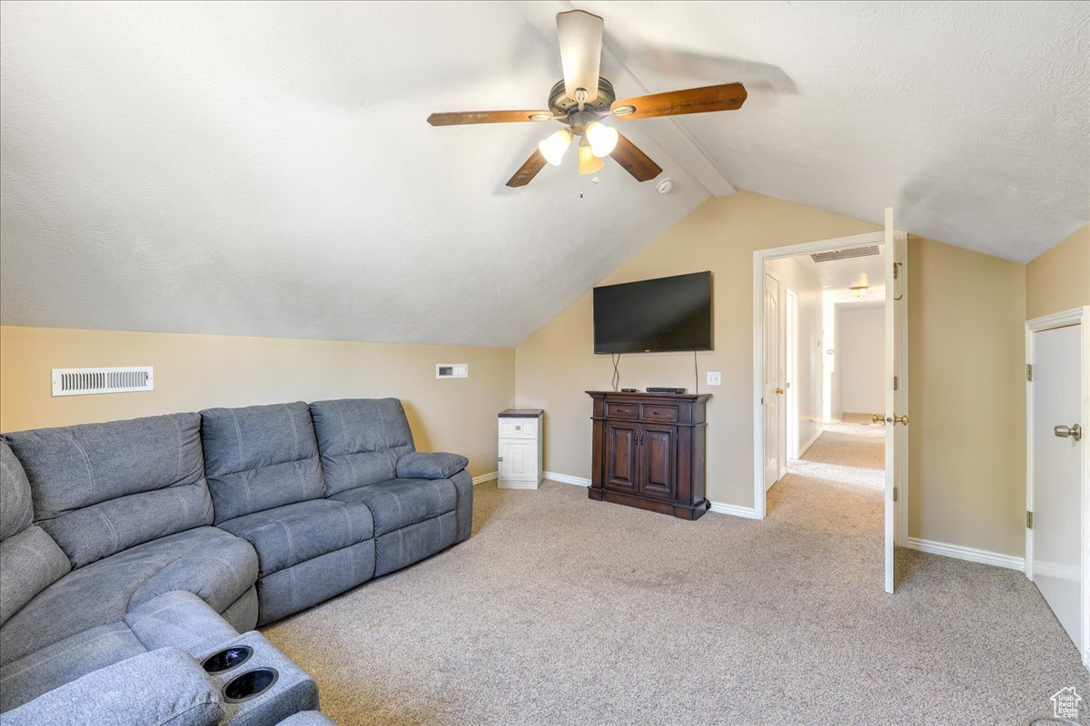 Living room featuring lofted ceiling, ceiling fan, and carpet