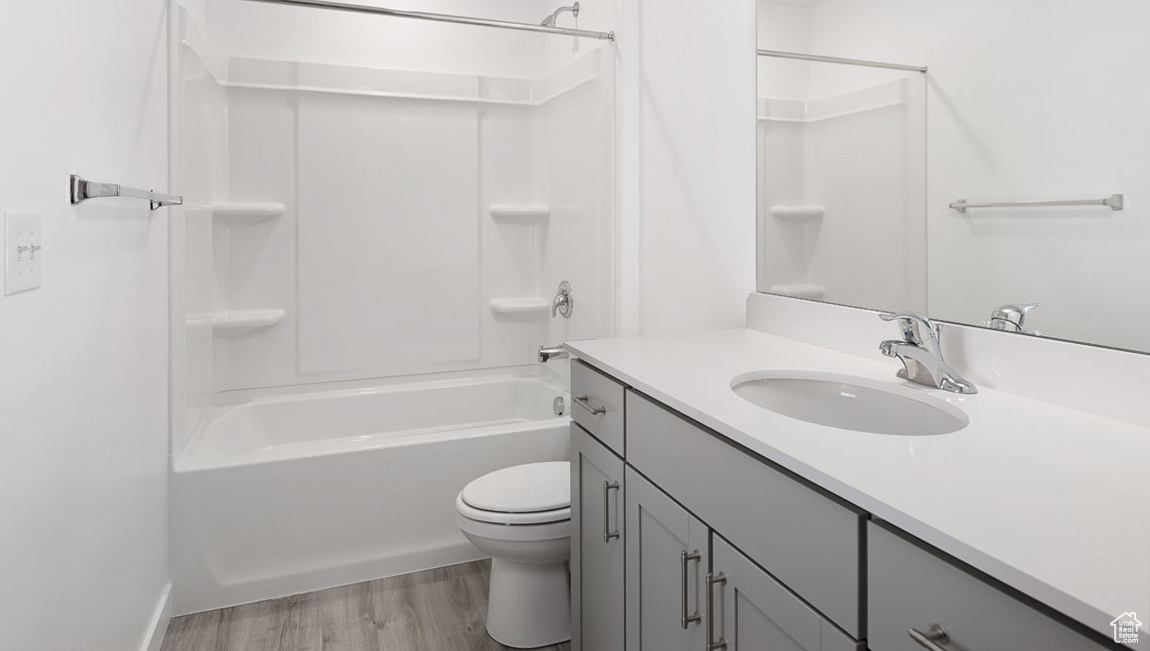 Full bathroom with wood-type flooring, shower / tub combination, vanity with extensive cabinet space, and toilet