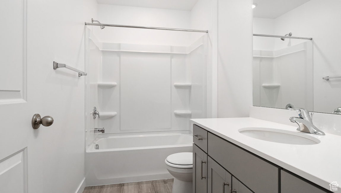 Full bathroom with wood-type flooring, washtub / shower combination, vanity, and toilet