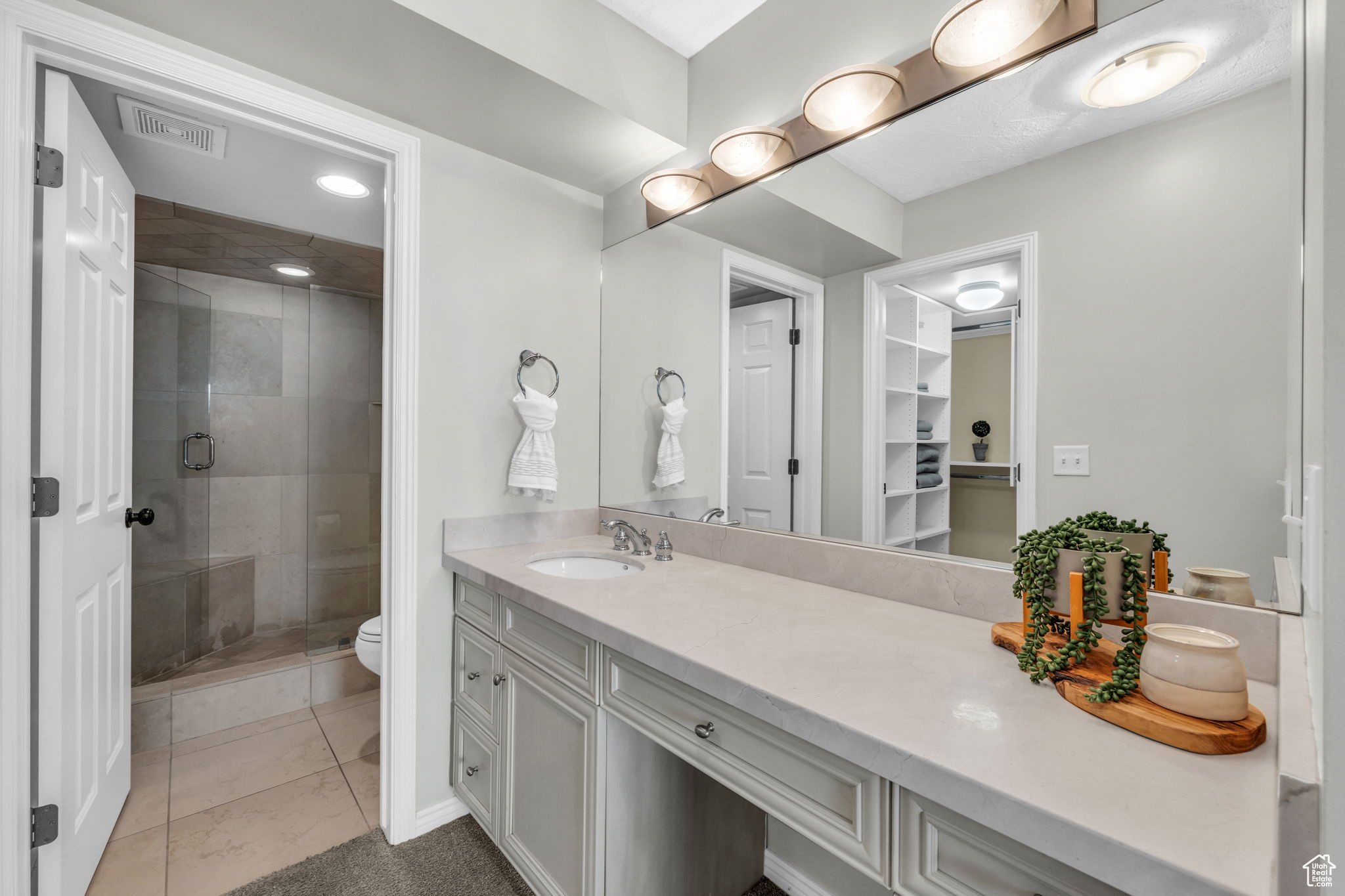 On suite bathroom with tile flooring, oversized vanity, toilet, and a shower with shower door