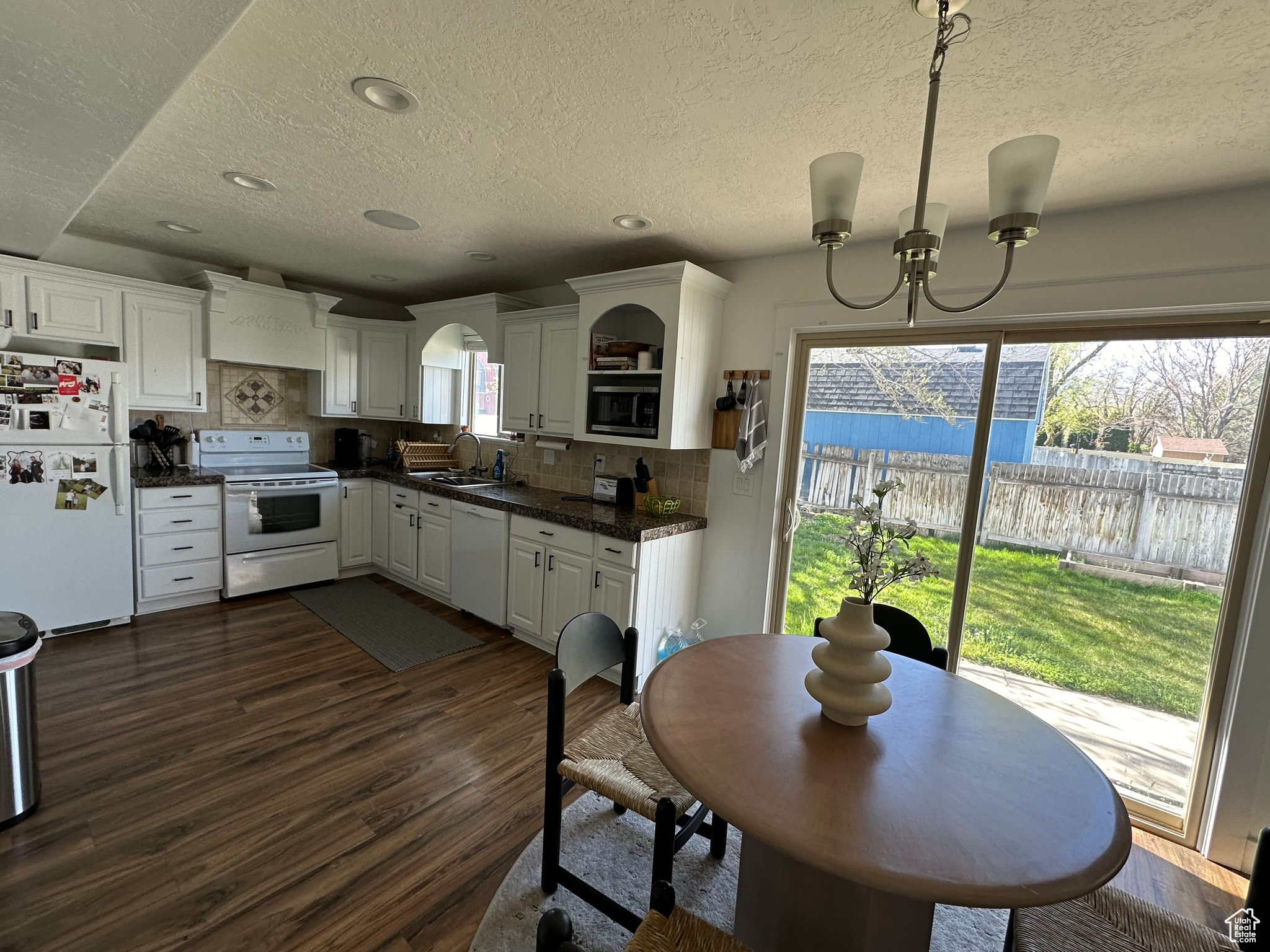 Kitchen with sink, white appliances, tasteful backsplash, white cabinetry, and dark wood-type flooring