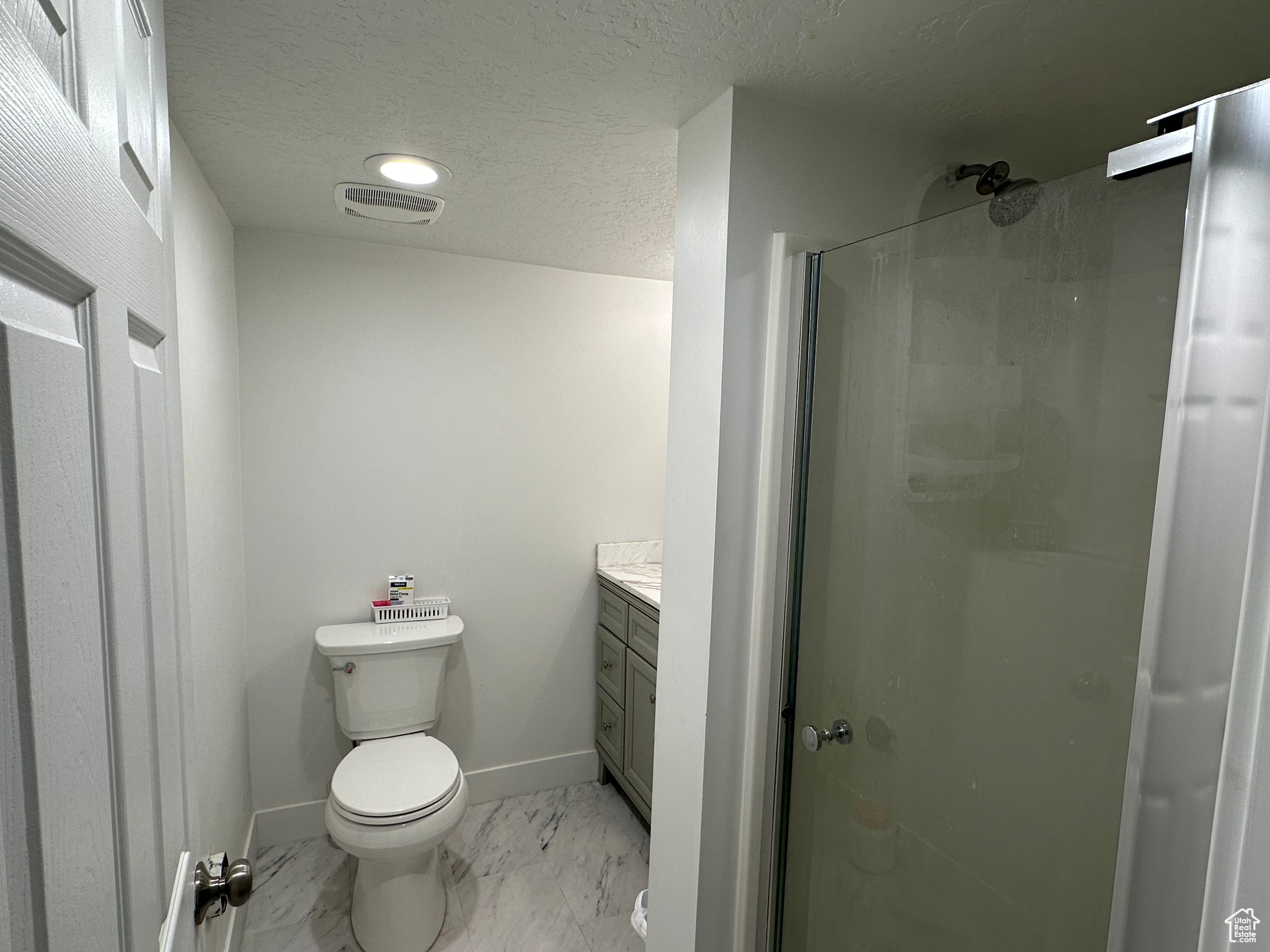 Bathroom featuring tile flooring, a textured ceiling, toilet, a shower with shower door, and vanity